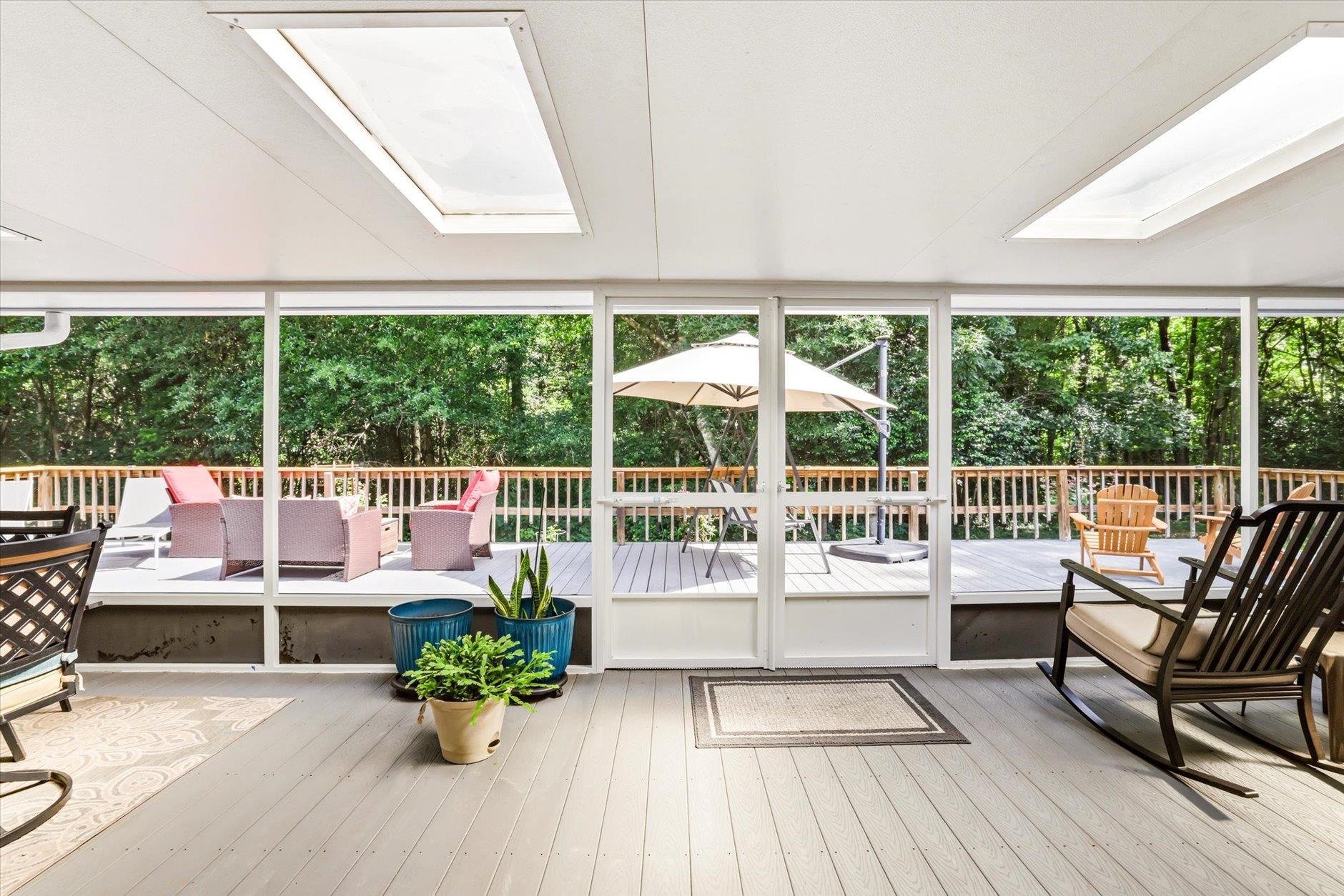 Screened porch with skylights, potted plants, and seating overlooking a tree-lined deck.