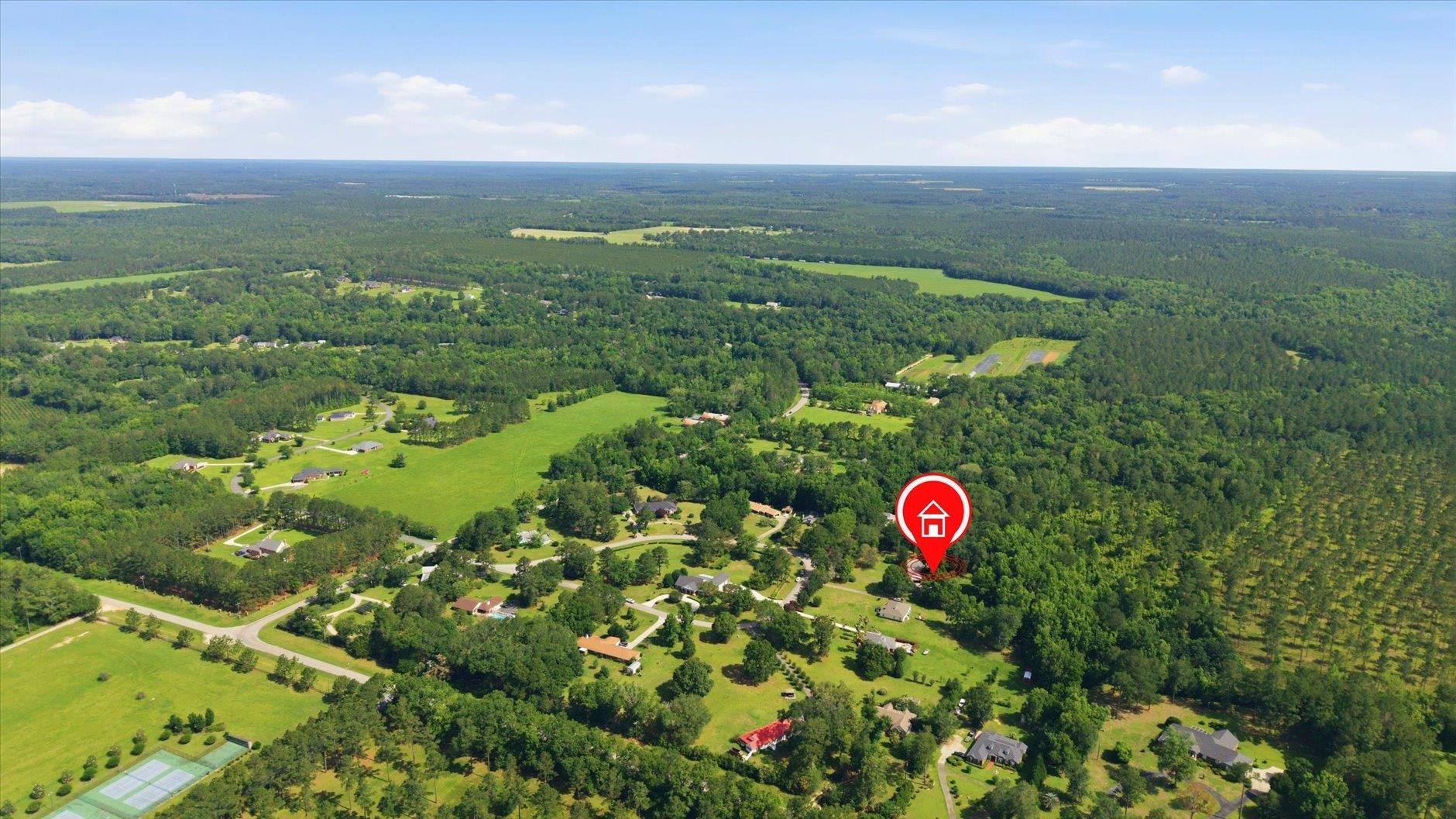Aerial view of a wooded rural neighborhood with scattered homes, green fields, and a red marker identifying the property.