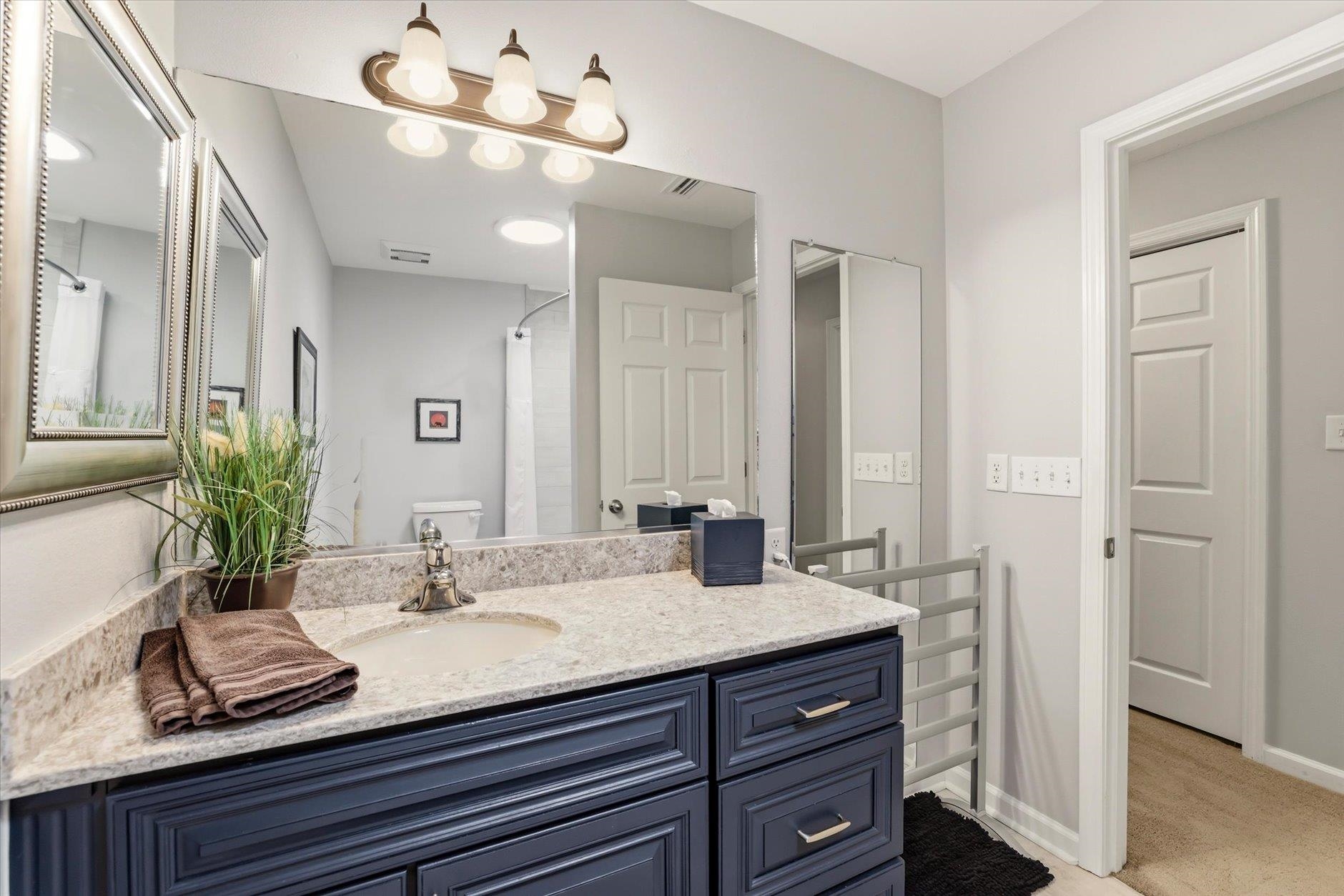 Bathroom with a dark blue vanity, pale stone countertop, and large mirrors.
