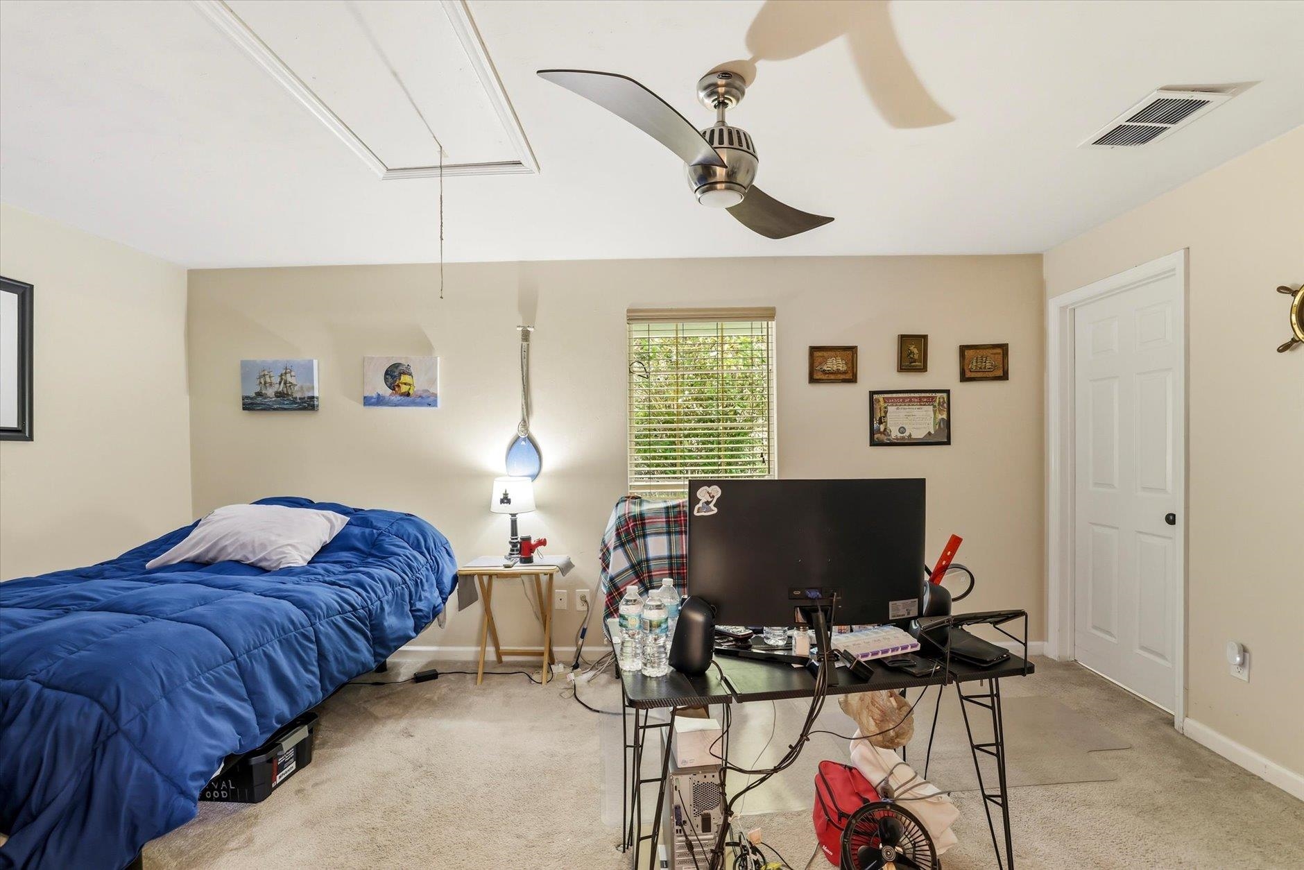 Bedroom with a blue-covered bed, computer desk, ceiling fan, and window with blinds.