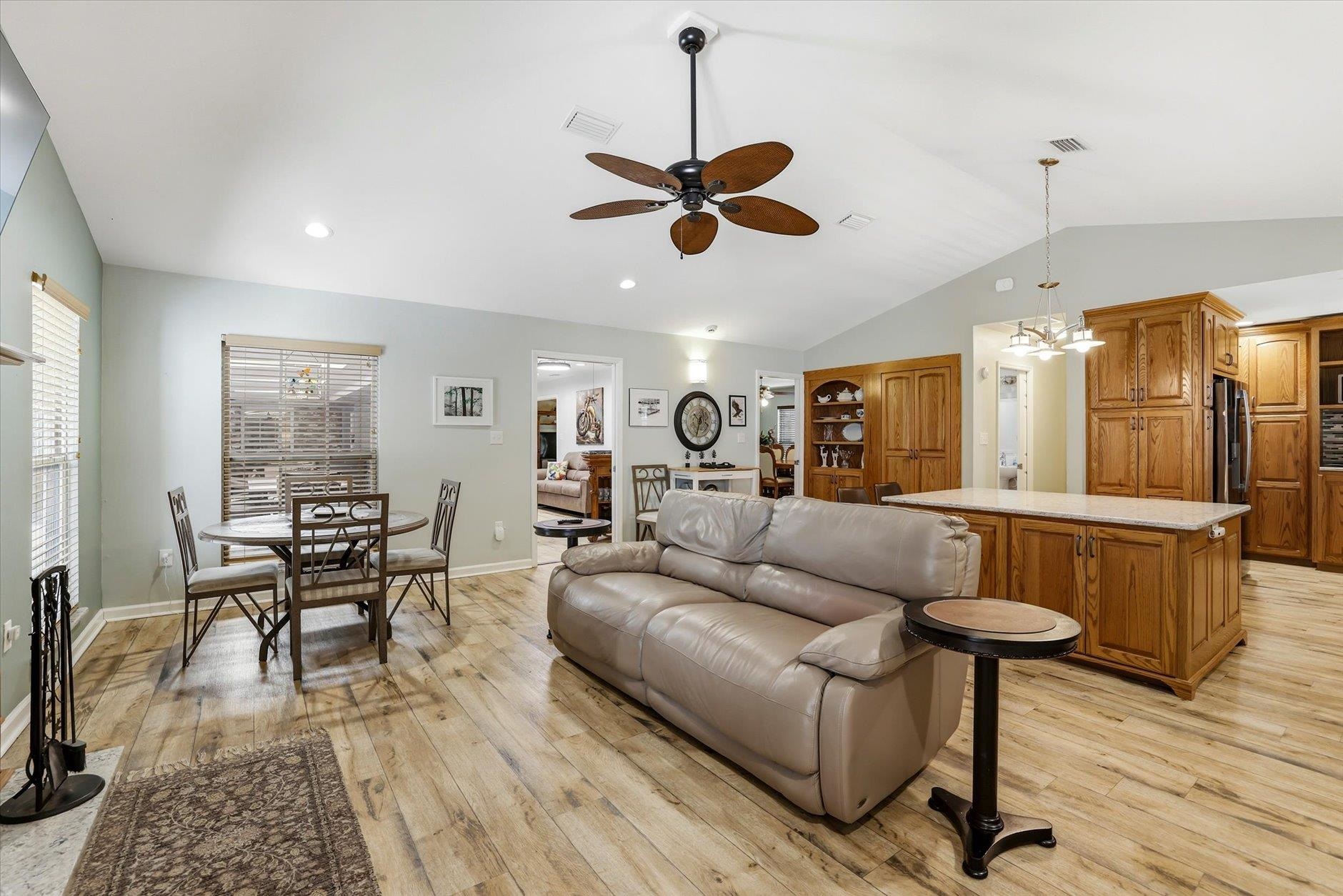 Open-plan living room, dining area, and kitchen with vaulted ceiling, gray sofa, and wood cabinetry.
