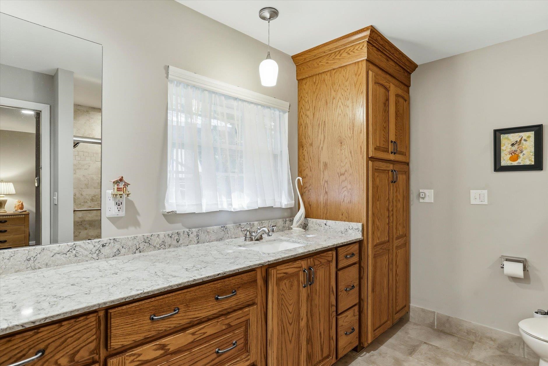 Bathroom vanity with a marble-look counter, oak cabinets, and a curtained window.
