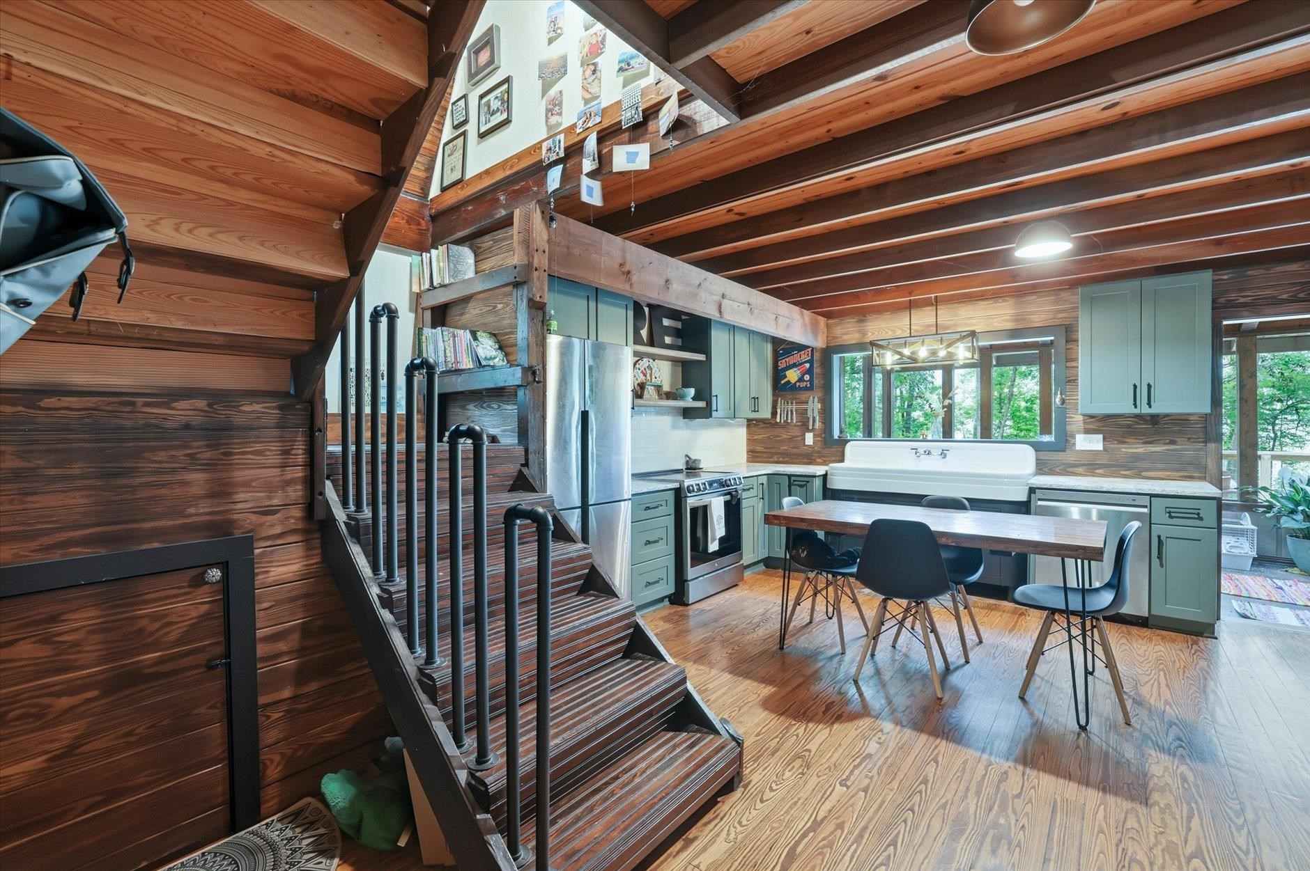 Kitchen and dining area with sage-green cabinets, a farmhouse sink, and a prominent wood staircase.