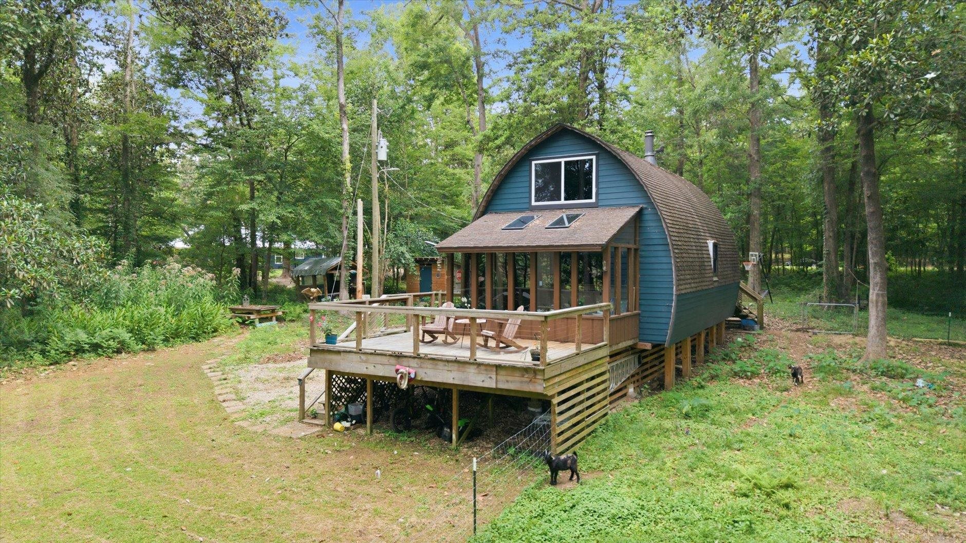 Blue A-frame cabin with a raised deck sits among mature trees.
