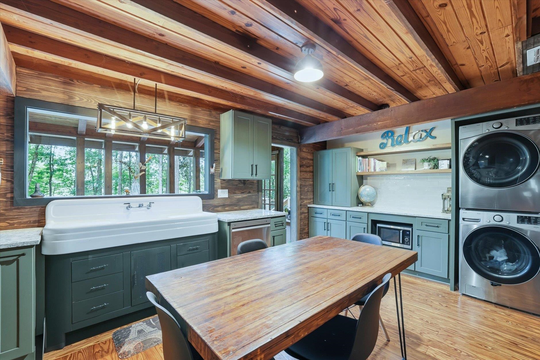 Laundry room with a large utility sink, blue-green cabinets, stacked washer and dryer, and exposed timber beams.