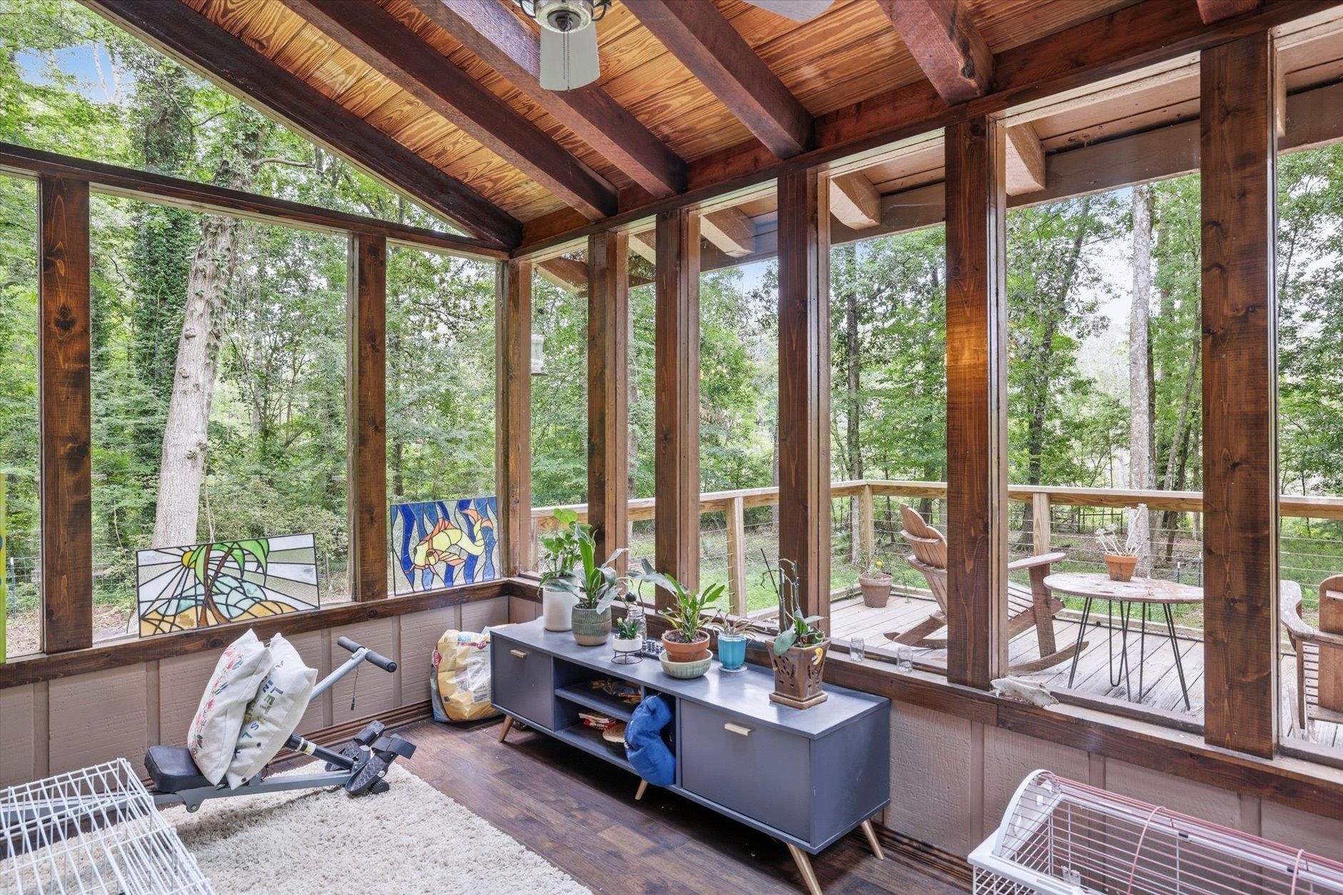 Sunroom with a vaulted timber ceiling, stained-glass panels, and windows overlooking a wooded deck.
