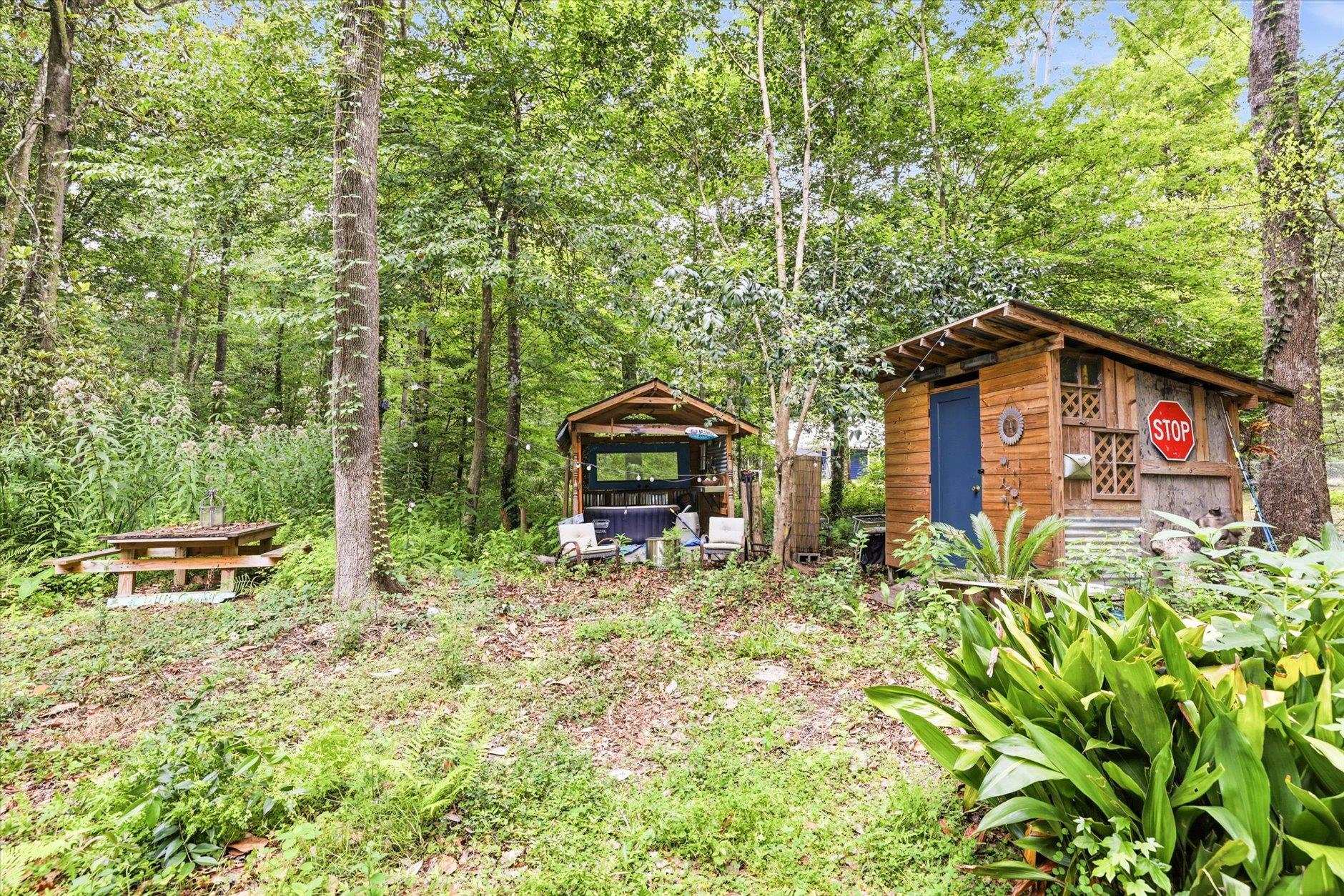 Wooded backyard with a wooden shed, covered seating area, and picnic table.