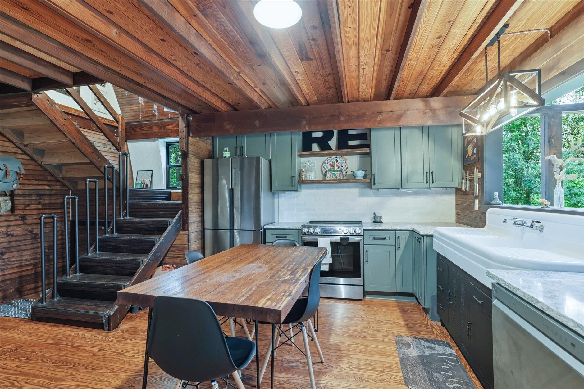 Kitchen with sage-green cabinets, farmhouse sink, wood ceilings, and an open staircase.