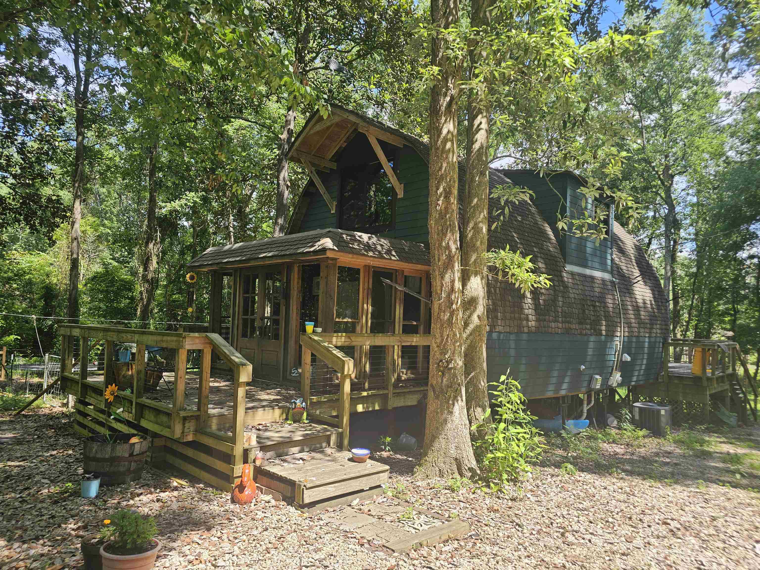 Green two-story cabin among trees, with a raised wooden porch and deck.