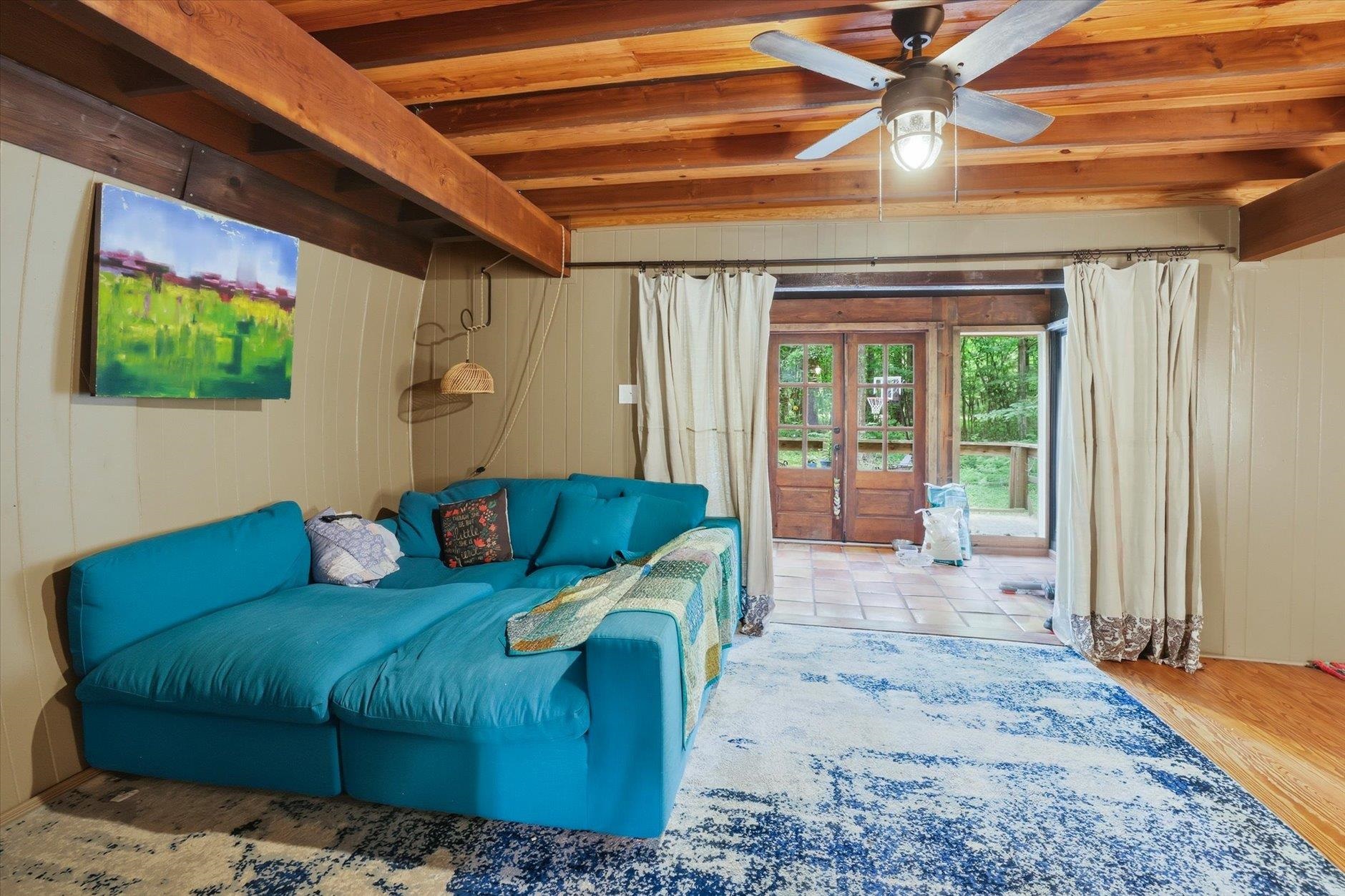 Living room with exposed wood beams, a teal sectional, and glass doors opening to the woods.