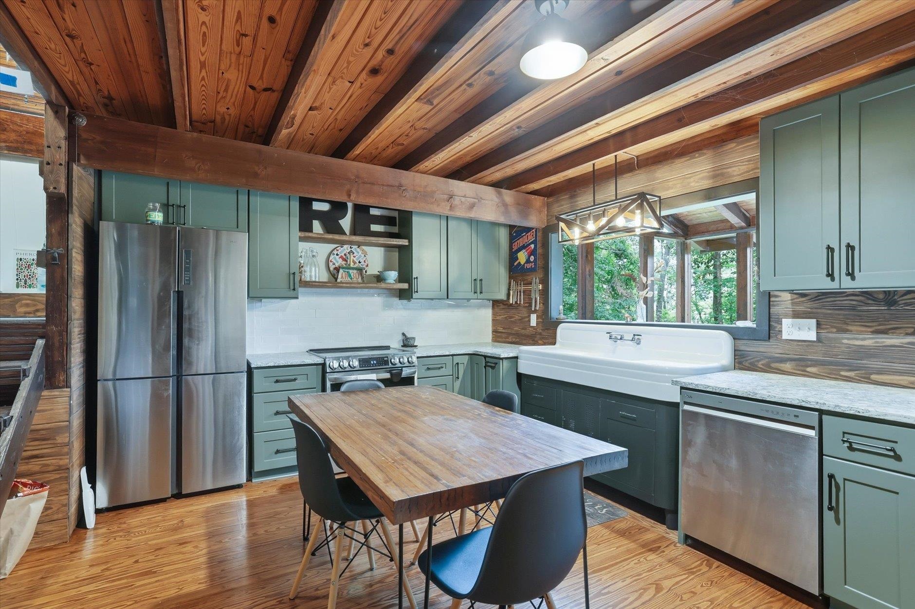 Kitchen with sage cabinets, farmhouse sink, stainless appliances, and exposed wood ceiling beams.
