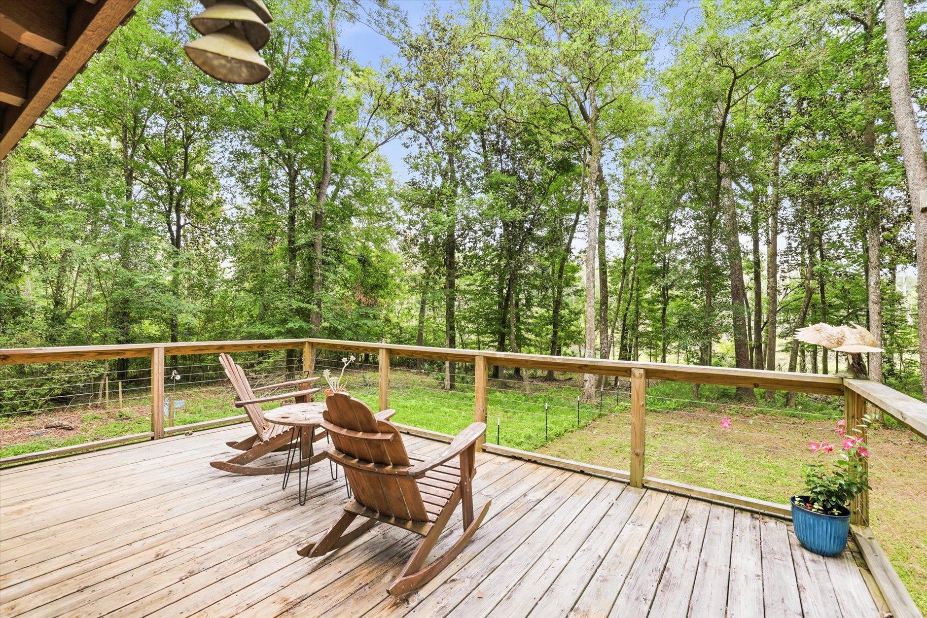 Wooden deck with Adirondack chairs overlooking a leafy wooded yard.