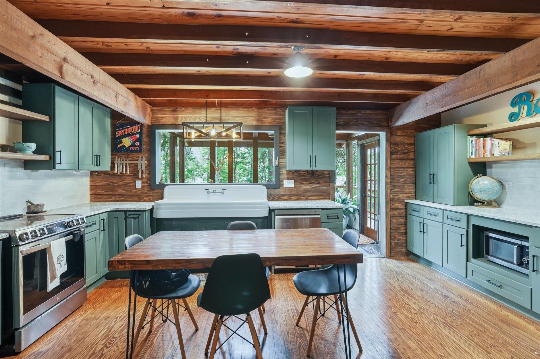 Kitchen and dining area with sage-green cabinets, exposed wood beams, and a long wooden table.