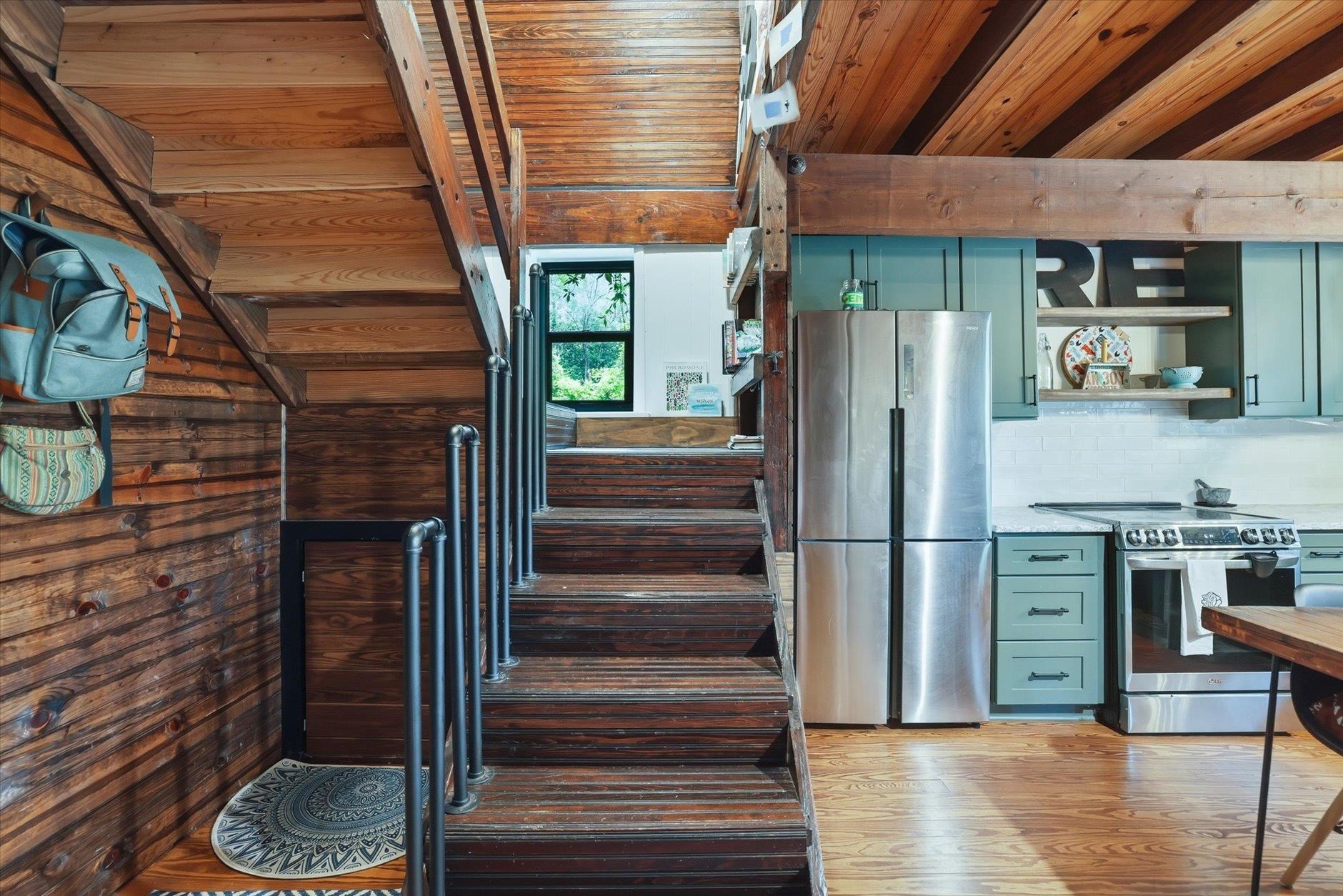 Kitchen with a dark wood staircase, exposed timber ceiling, teal cabinets, and stainless-steel appliances.