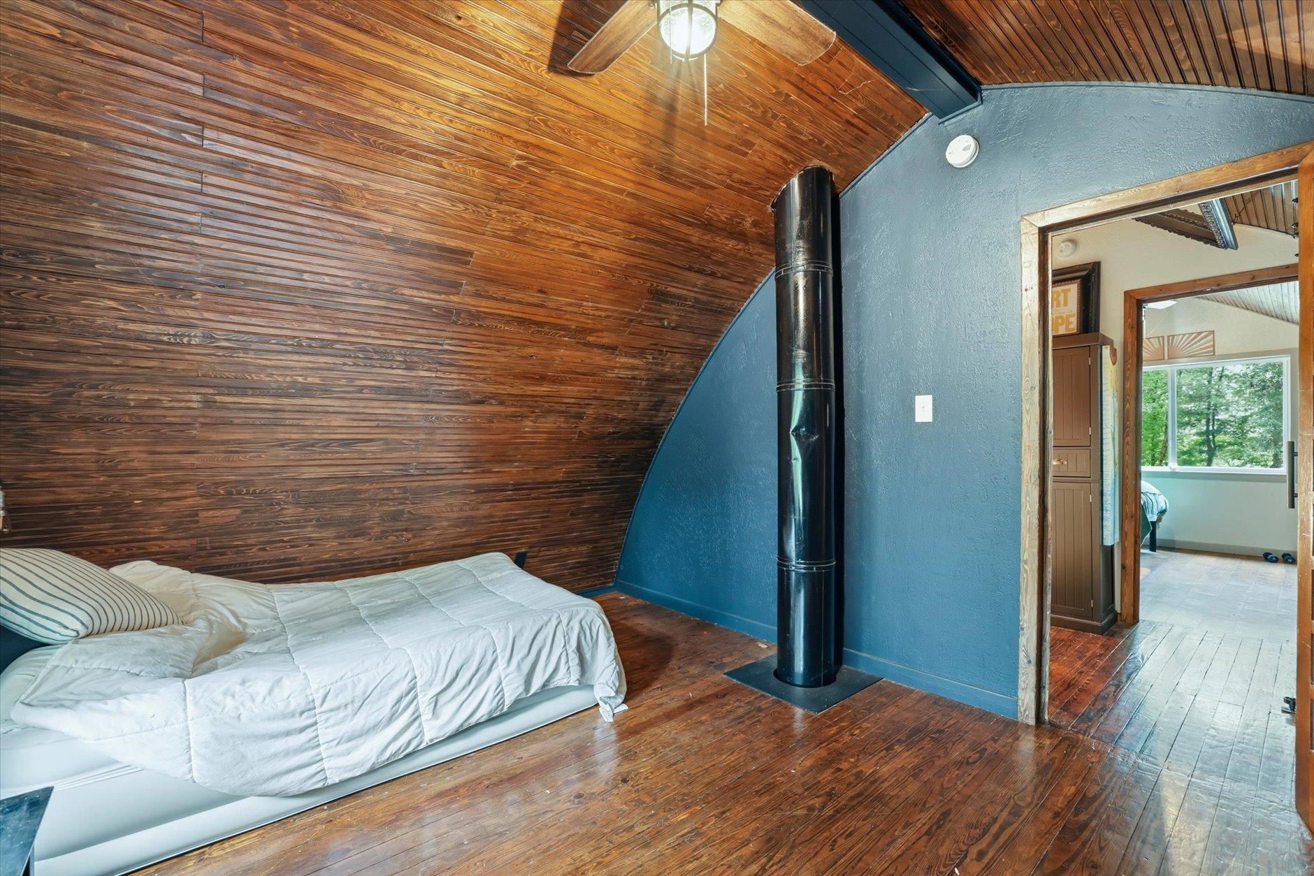 Attic bedroom with sloped wood-paneled walls, a low bed, and a black stove pipe.