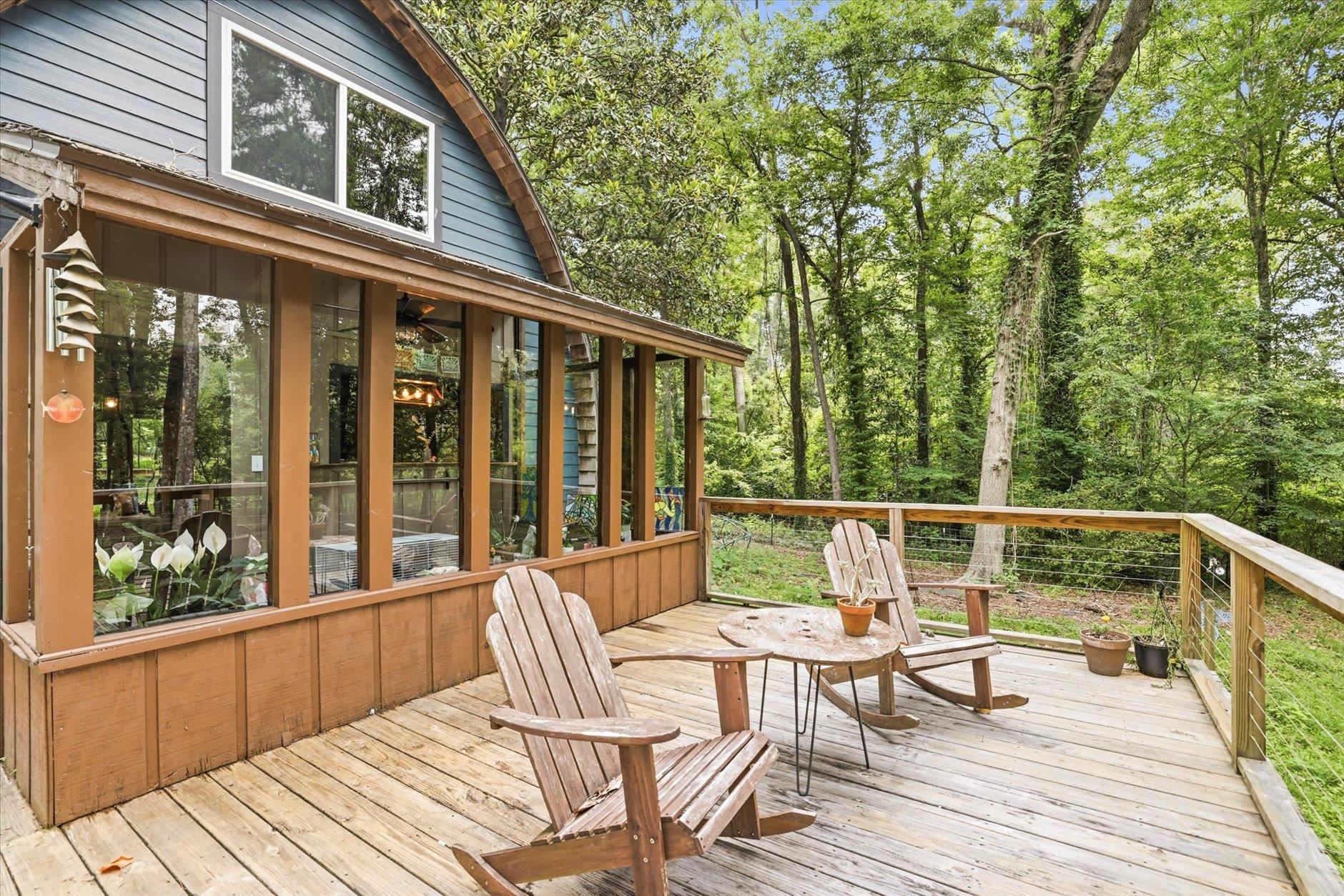Wooden deck with Adirondack chairs beside a blue-sided home, overlooking leafy woods.