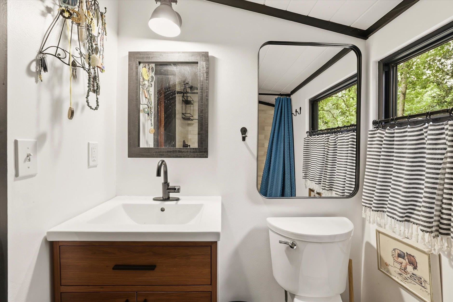 Bathroom with a wood vanity, white sink, striped shower curtain, and black ceiling beams.