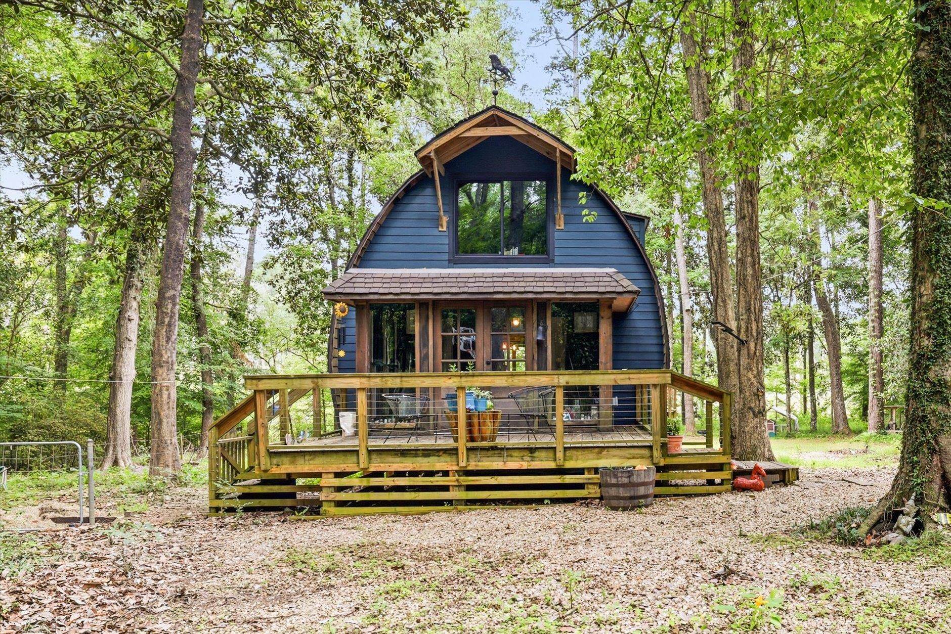Blue barn-style house with a raised wooden deck nestled among mature trees.