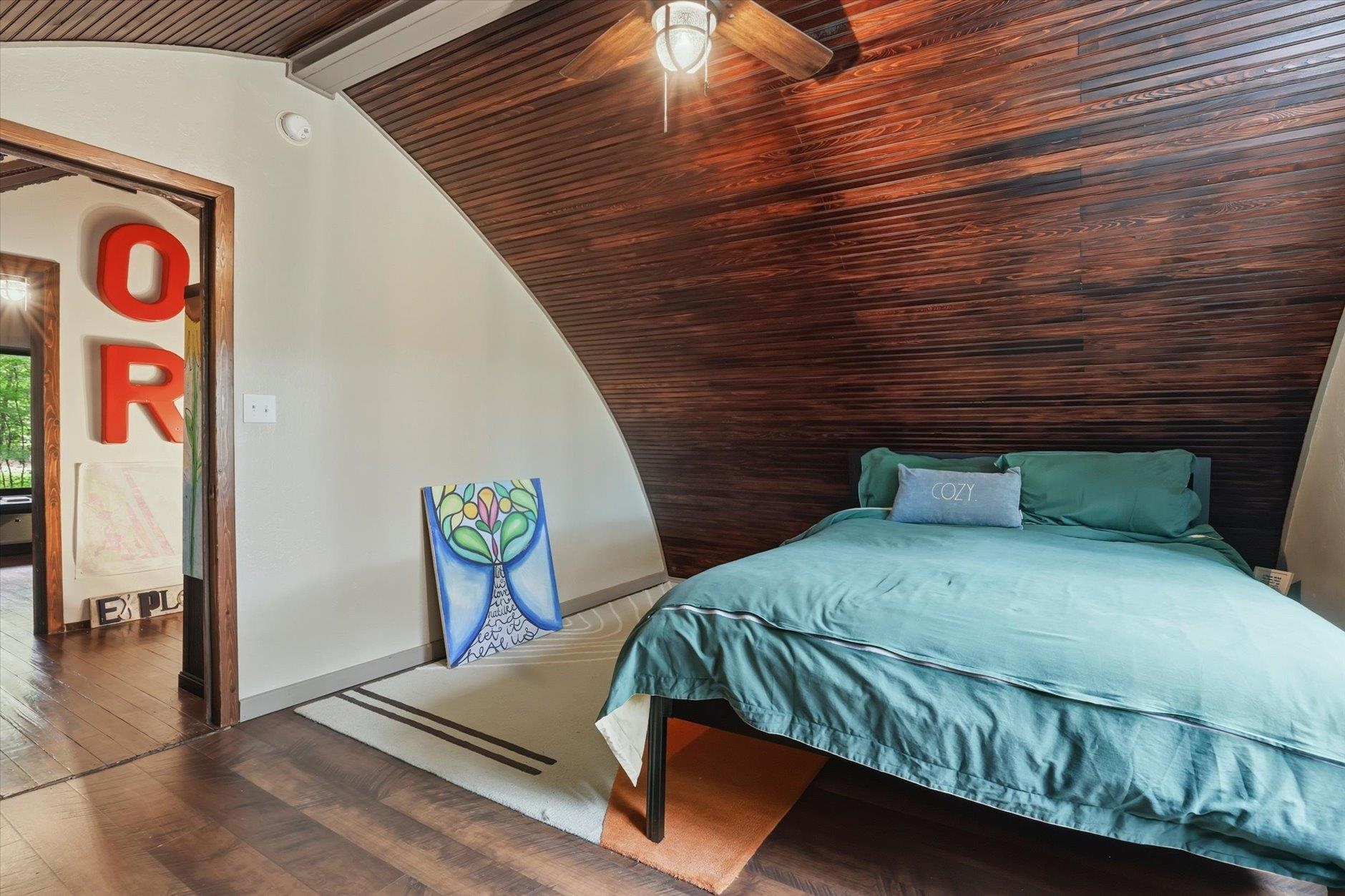 Bedroom with a teal bed beneath a dramatic dark wood sloped ceiling and ceiling fan.