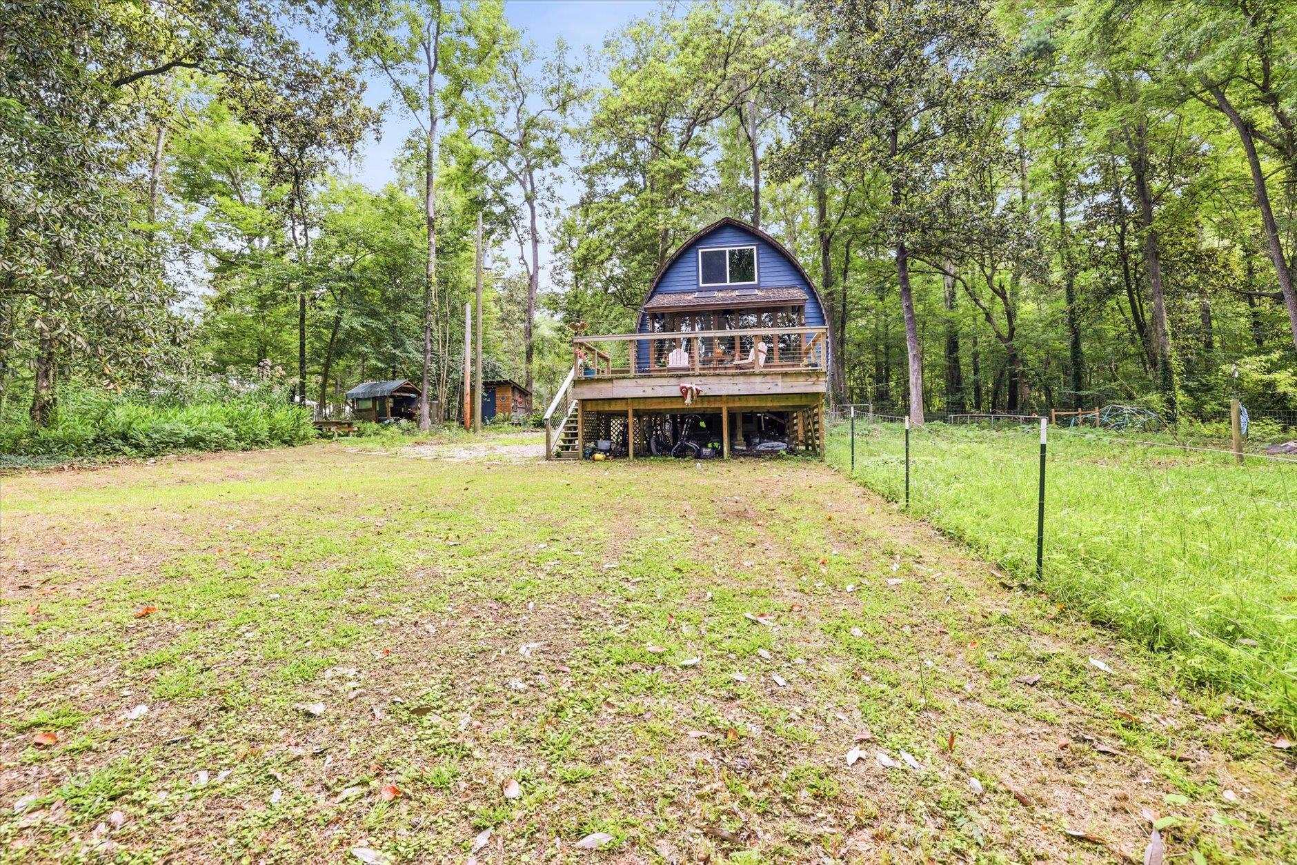 Blue arched-roof cabin with a raised deck sits in a leafy wooded yard.