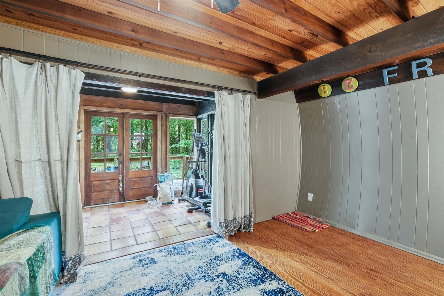 Room with vaulted wood ceiling, French doors to a wooded area, and exercise equipment.