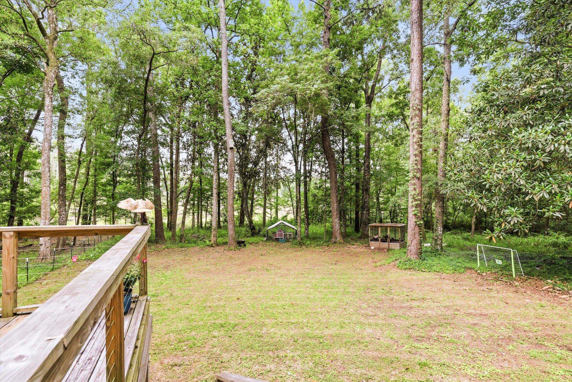 Wooded backyard with a grassy clearing, mature trees, and a wooden deck railing.