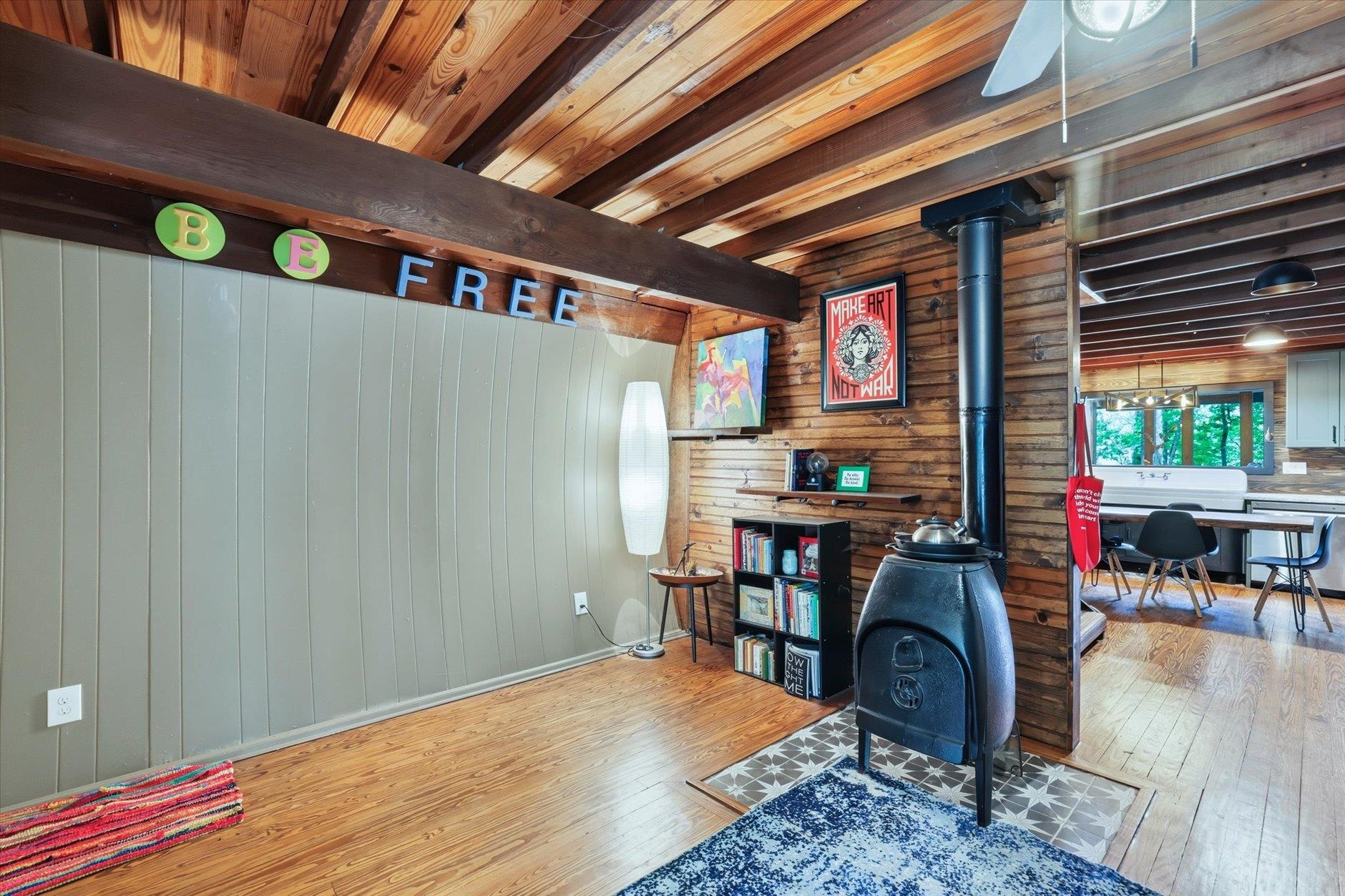 Wood-paneled living area with exposed beams, a freestanding stove, hardwood floors, and adjoining dining space.
