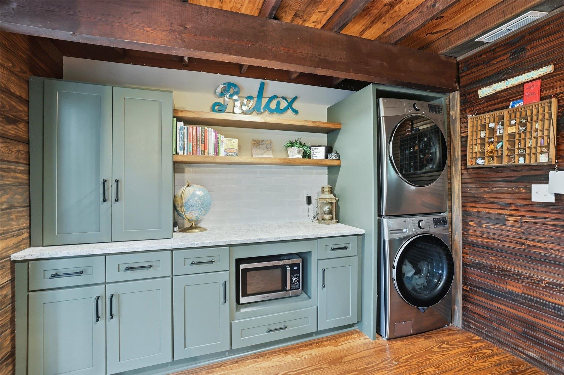 Laundry room with sage-green cabinets, open shelves, and stacked washer and dryer.