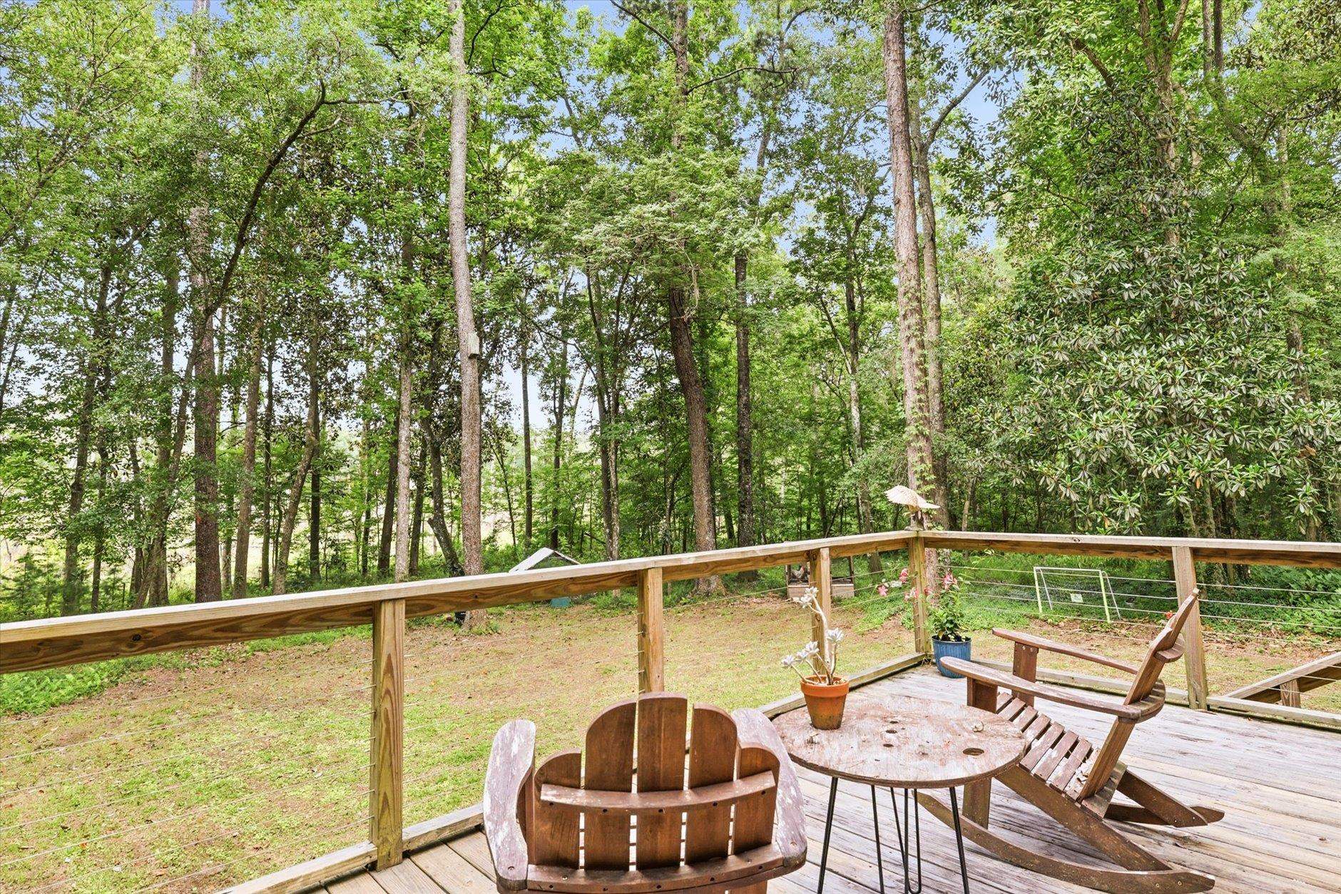 Wooden deck with Adirondack chairs overlooking a leafy wooded yard.