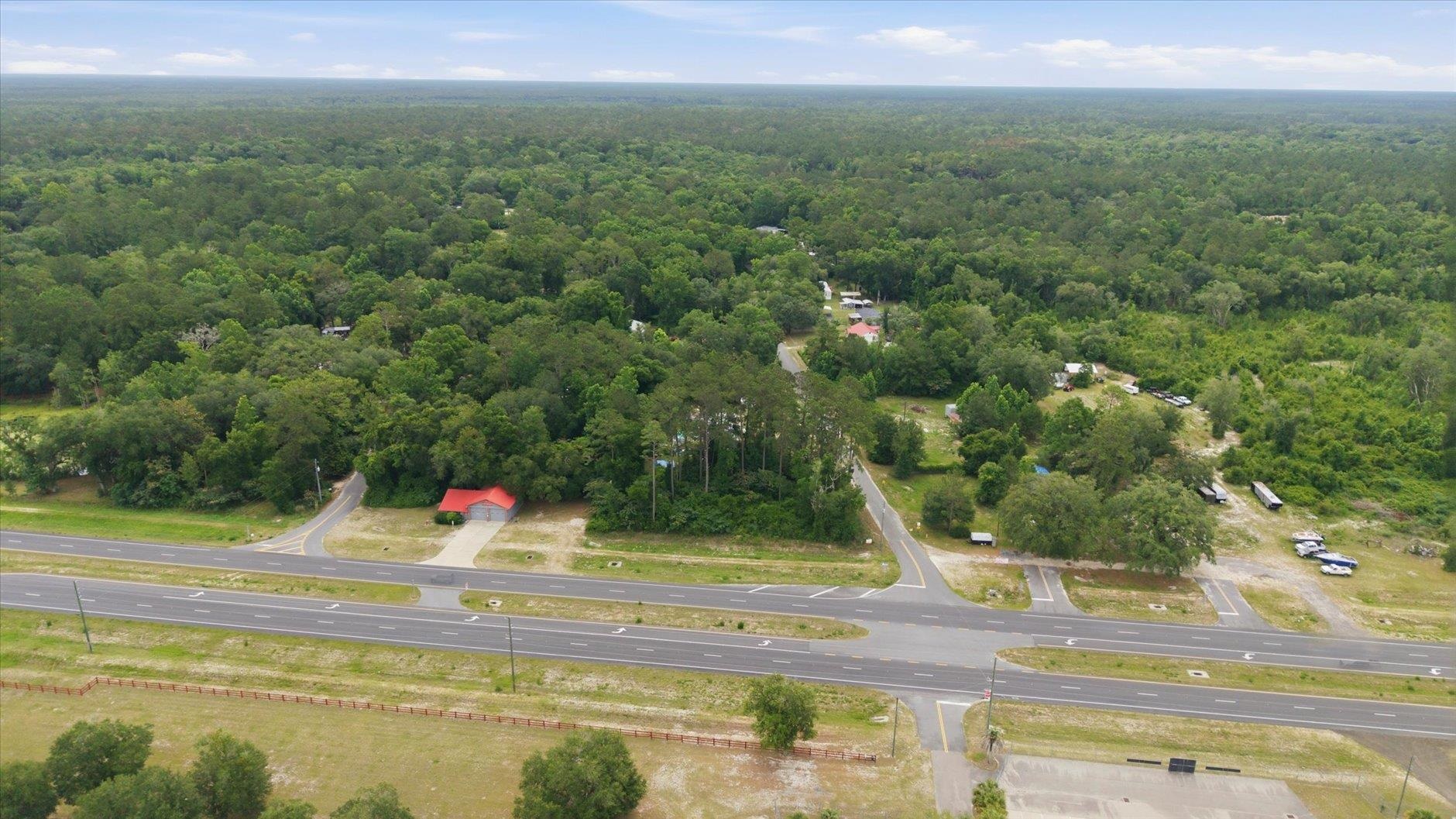 Aerial view of wooded land beside a highway, with an intersection and scattered buildings.