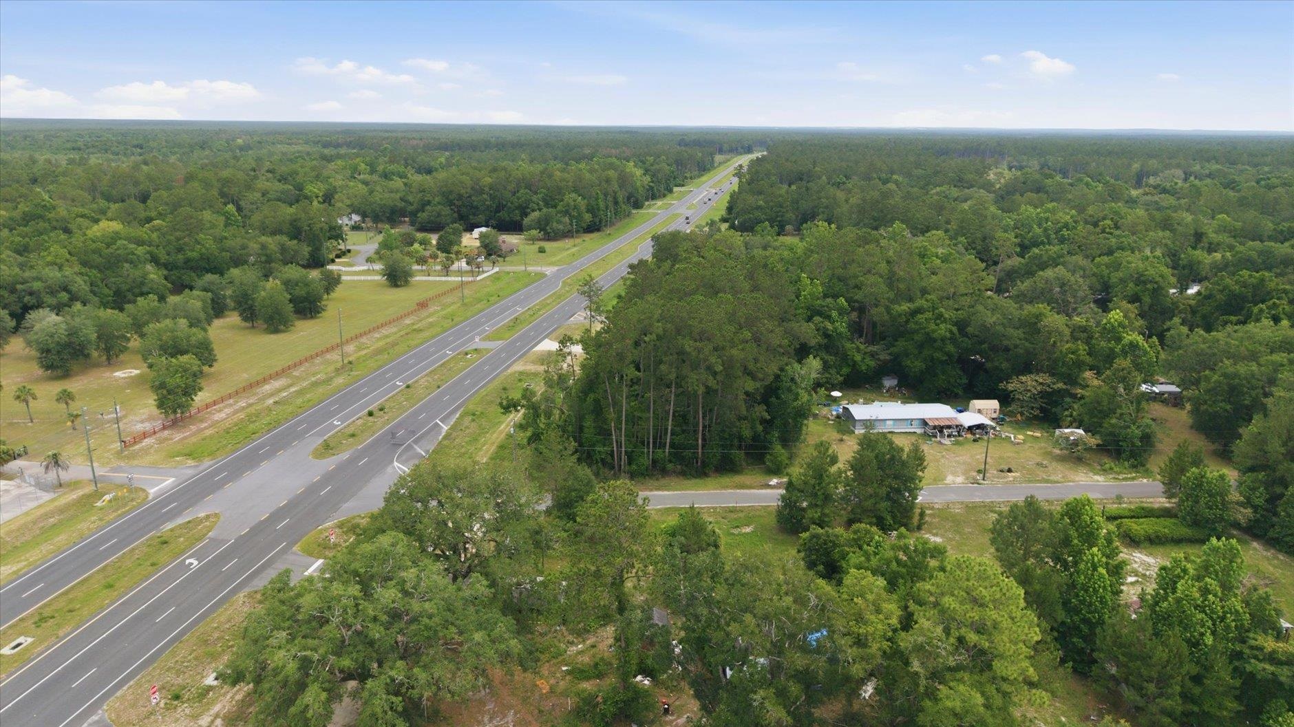 Aerial view of wooded land beside a divided highway, with a grassy clearing and buildings.