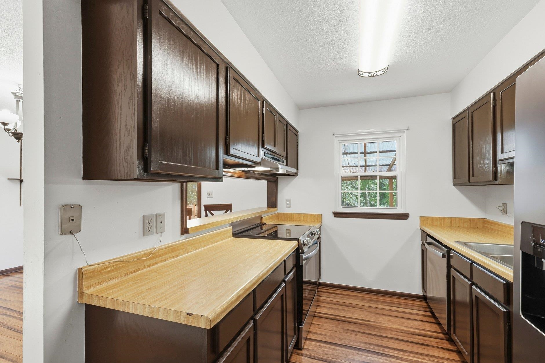 Kitchen with dark wood cabinets, butcher-block counters, stainless appliances, and striped wood flooring.