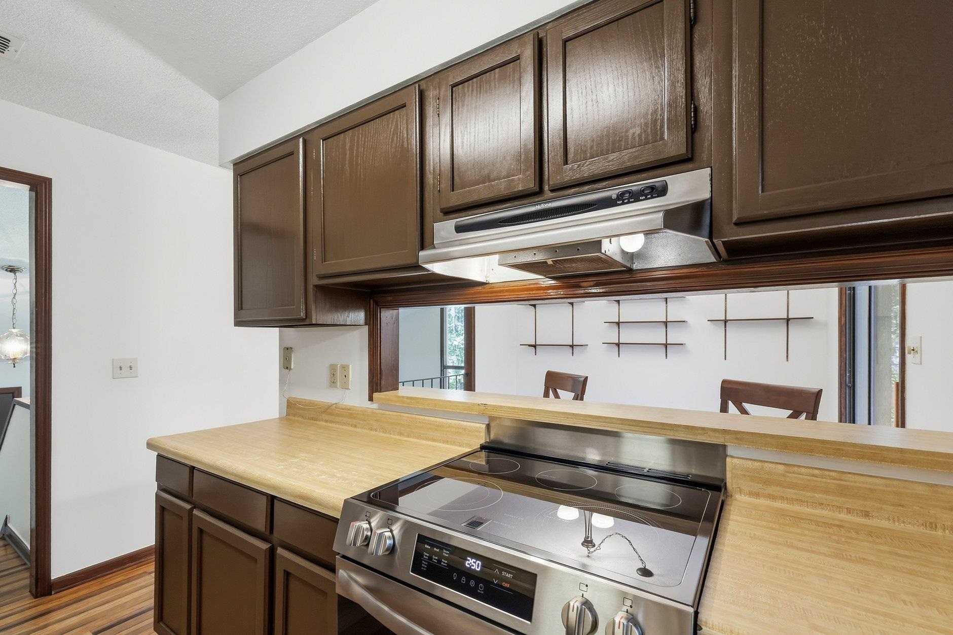 Kitchen with dark wood cabinets, wood countertops, and a stainless steel range beneath a pass-through.