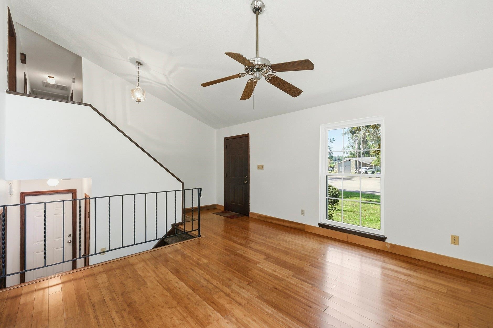 Empty upper-level living area with hardwood floors, a ceiling fan, and railing overlooking the entry.