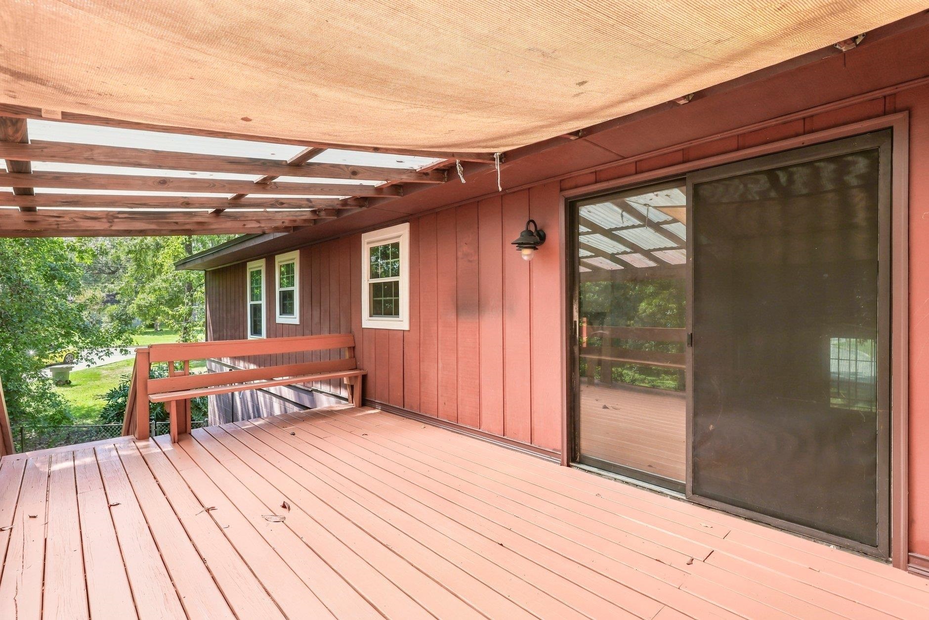 Covered wooden deck with red siding, overhead slats, and sliding glass doors.