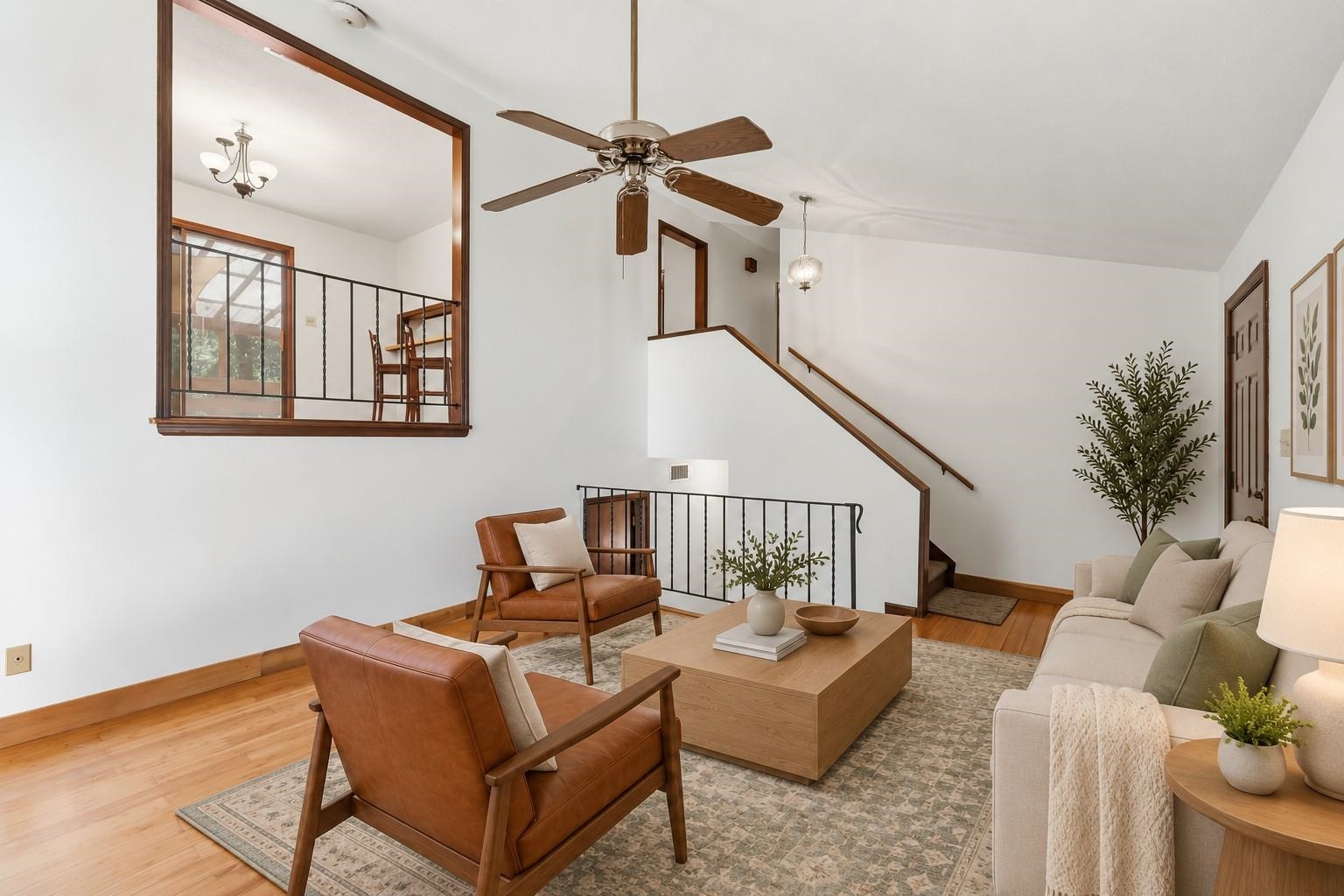 Living room with vaulted ceiling, wood fan, staircase, and an upper-level railing overlooking the seating area.