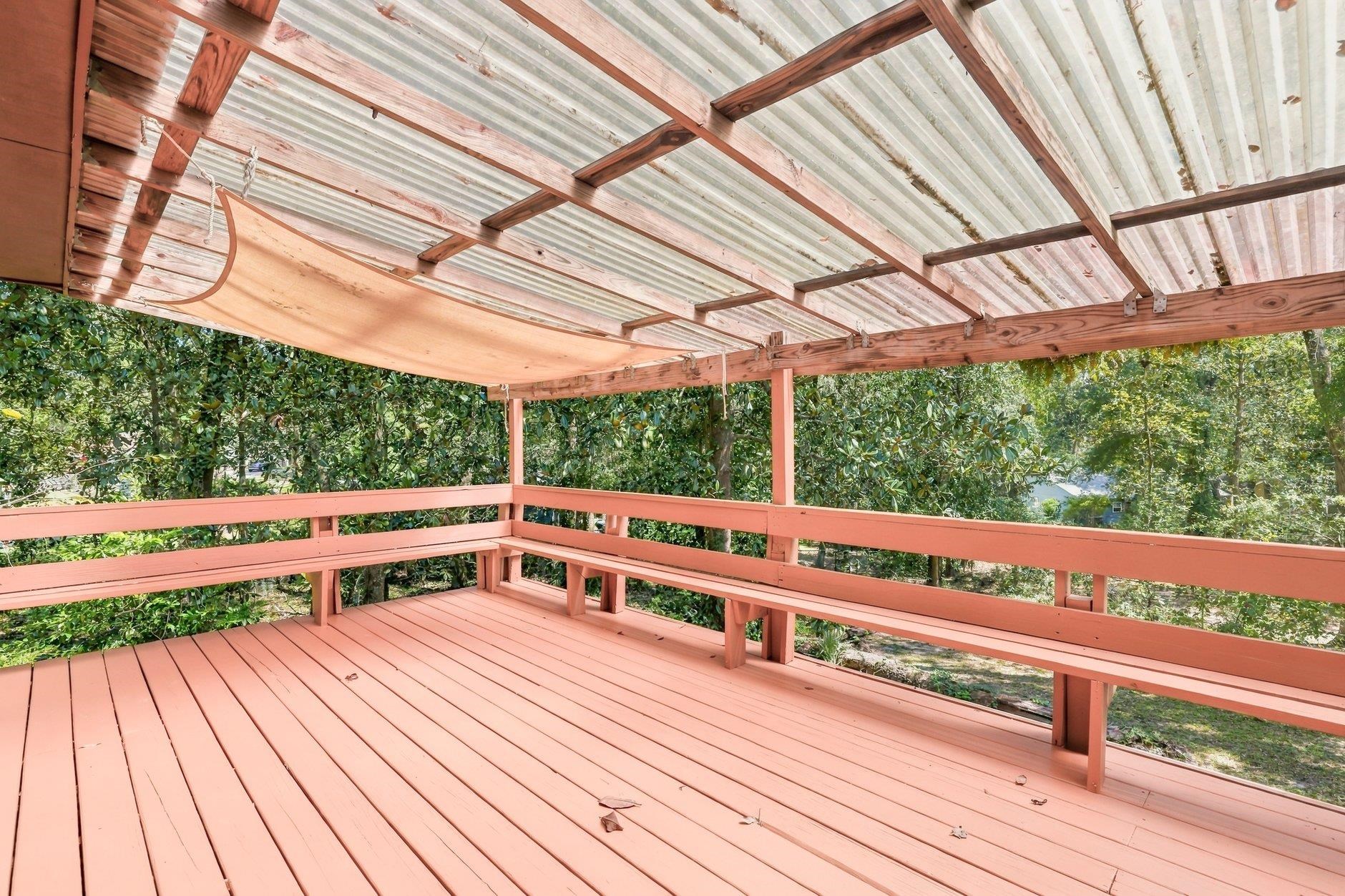 Covered wooden deck with salmon-pink boards and railings, surrounded by trees.