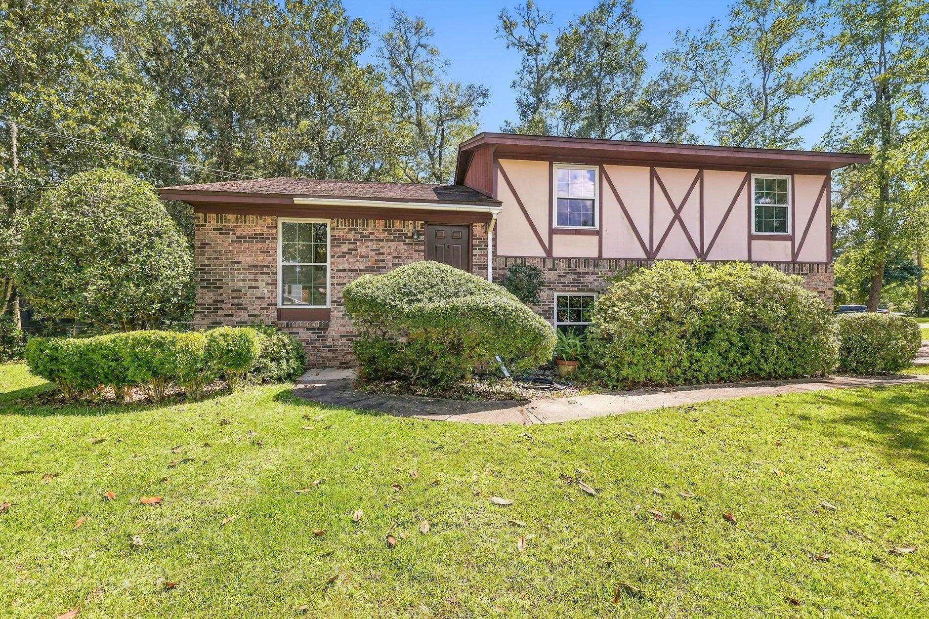 Split-level brick-and-siding home with timber-style trim, trimmed shrubs, and a broad front lawn.