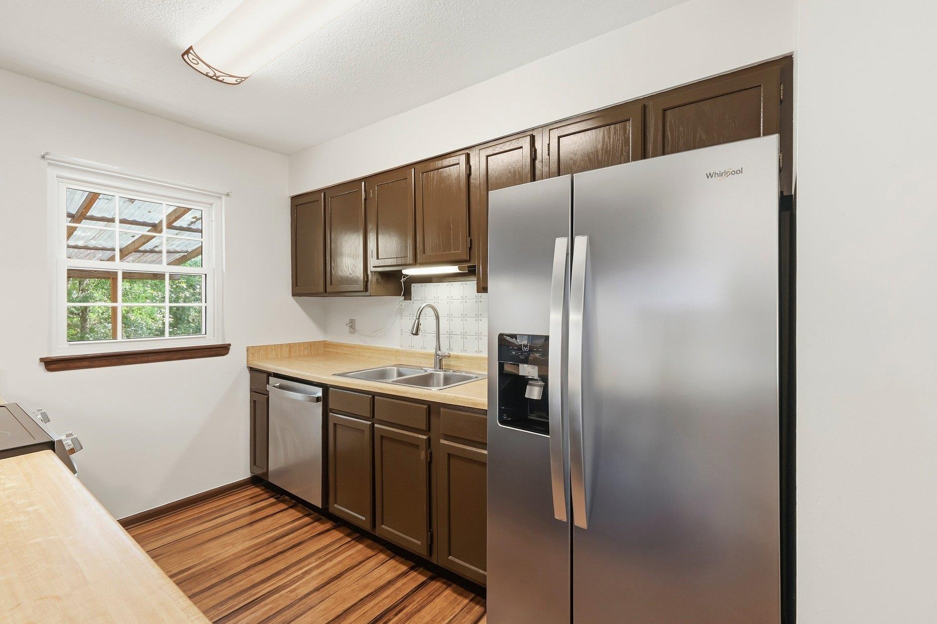 Kitchen with dark cabinets, stainless steel appliances, and a window overlooking greenery.