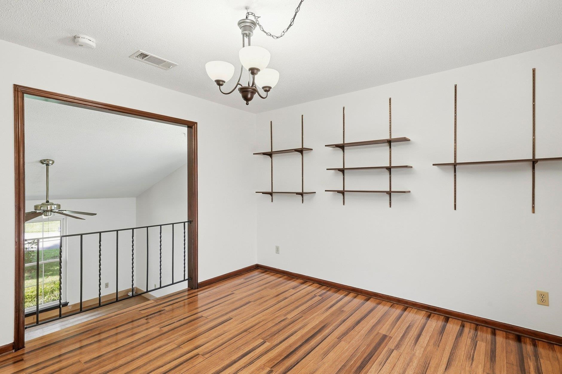 Upstairs room with hardwood floors, wall-mounted shelves, and an open railing overlooking the lower level.