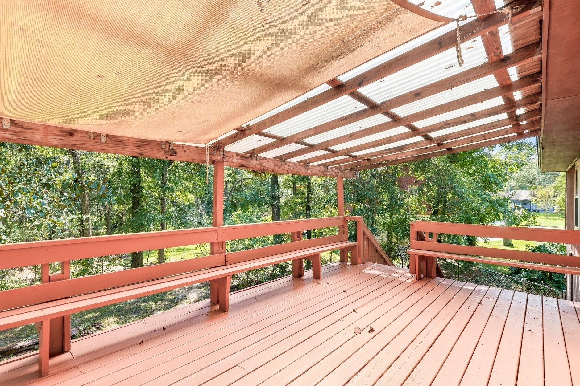 Covered wooden deck with salmon-colored railings overlooking a leafy yard.