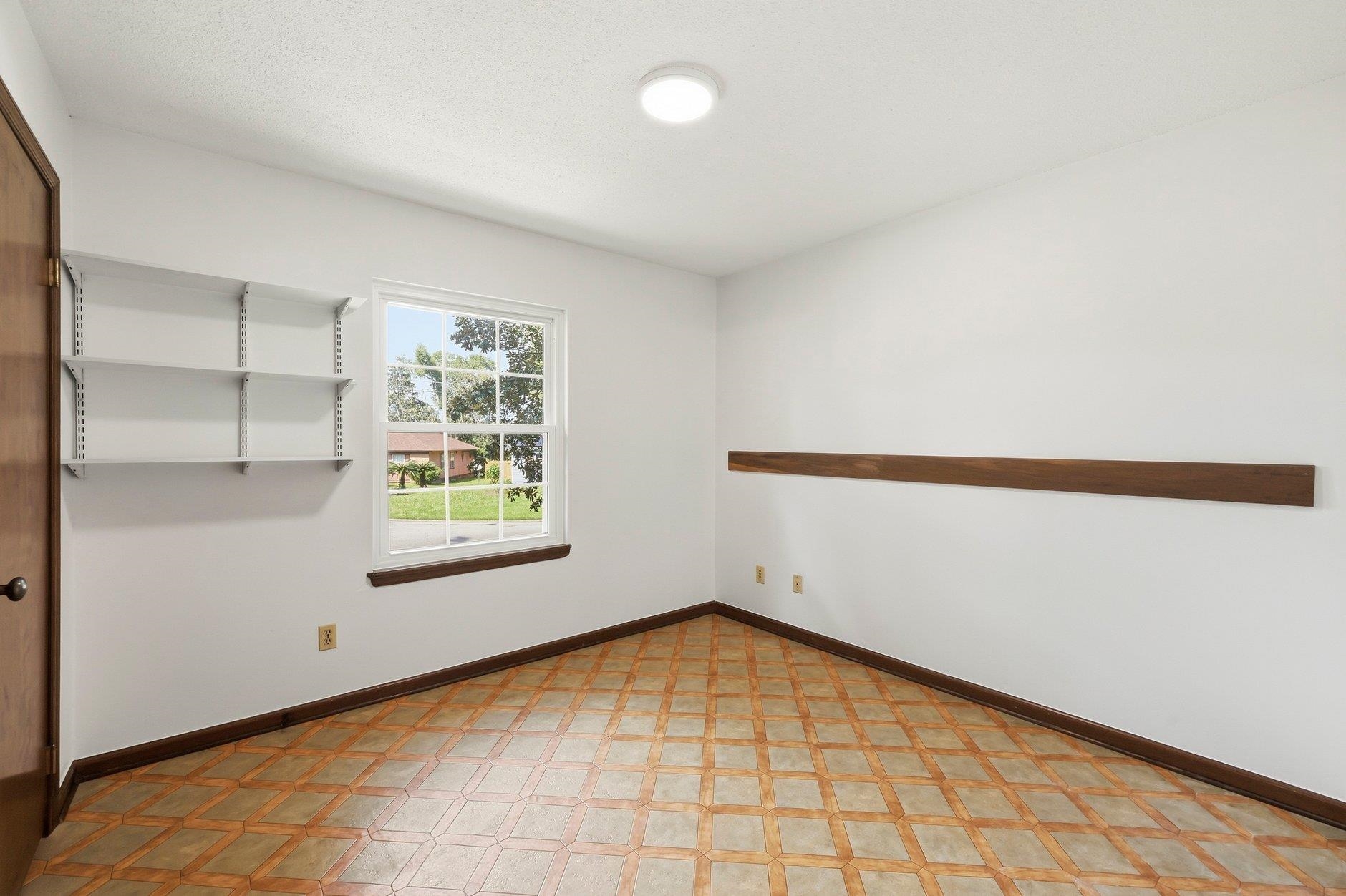 Empty room with wall shelves, patterned tile flooring, and a window overlooking a lawn.