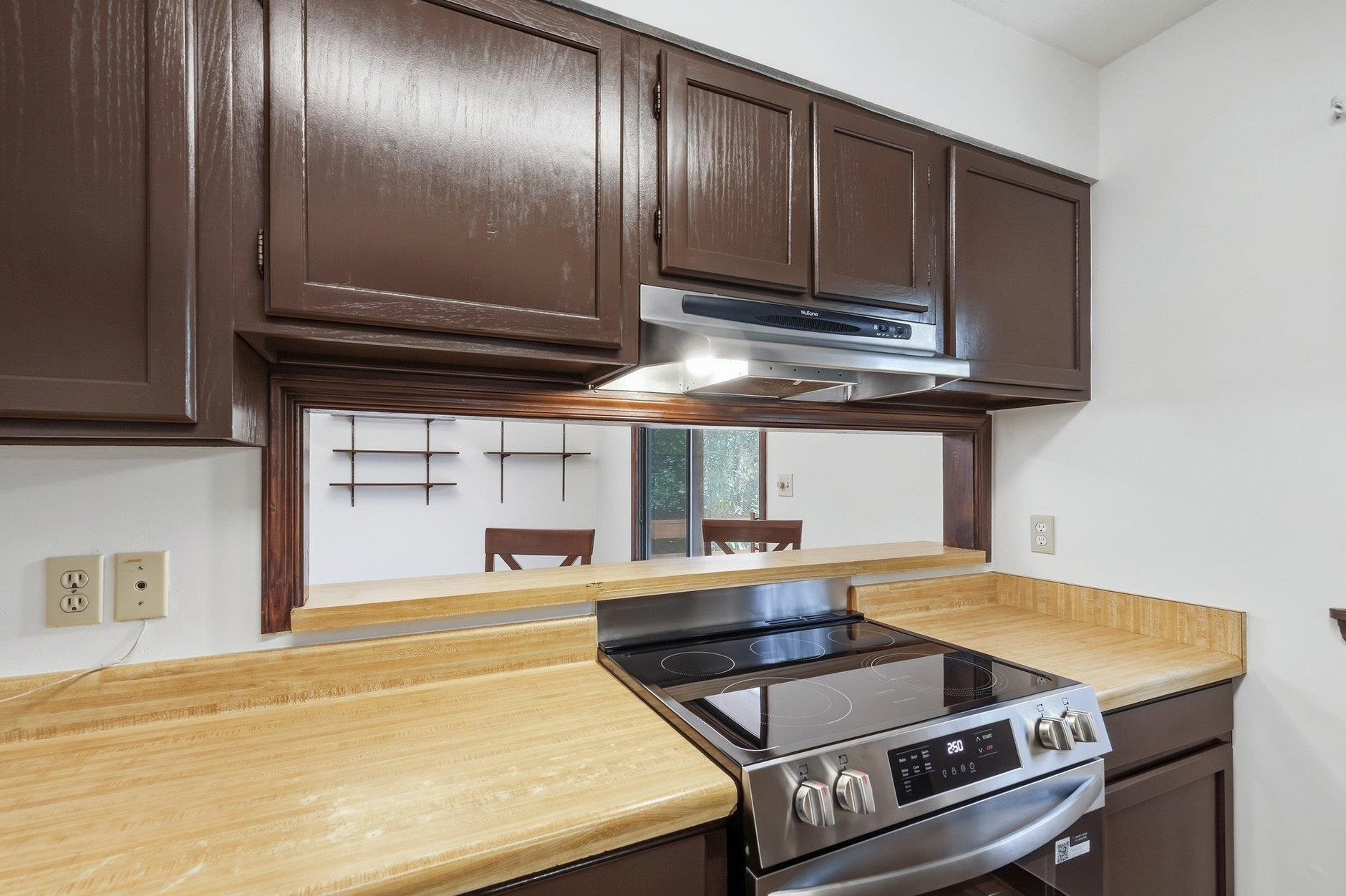 Kitchen with dark cabinets, light wood countertops, and a stainless steel electric range beneath a pass-through.