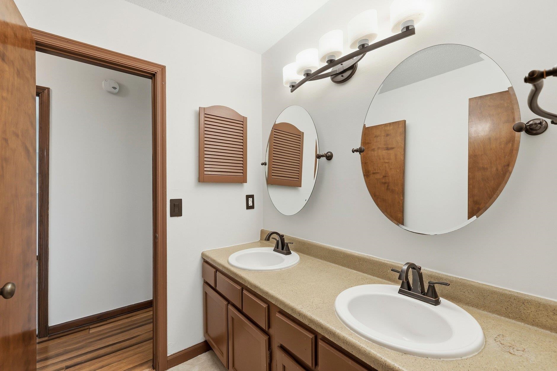 Bathroom with a double-sink brown vanity, beige countertop, and large oval mirrors.