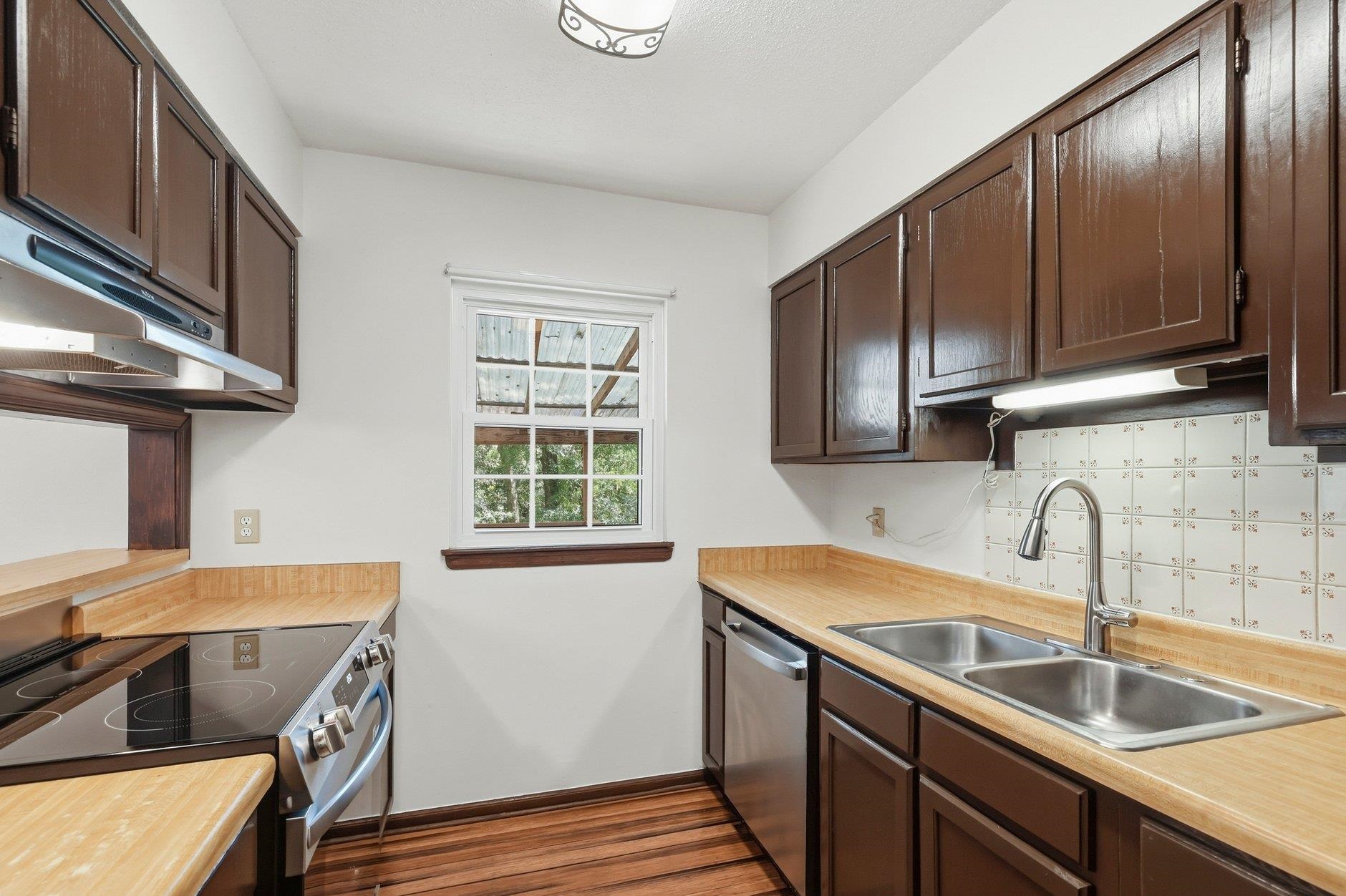 Kitchen with dark brown cabinets, light wood counters, and a stainless double sink beneath a window.