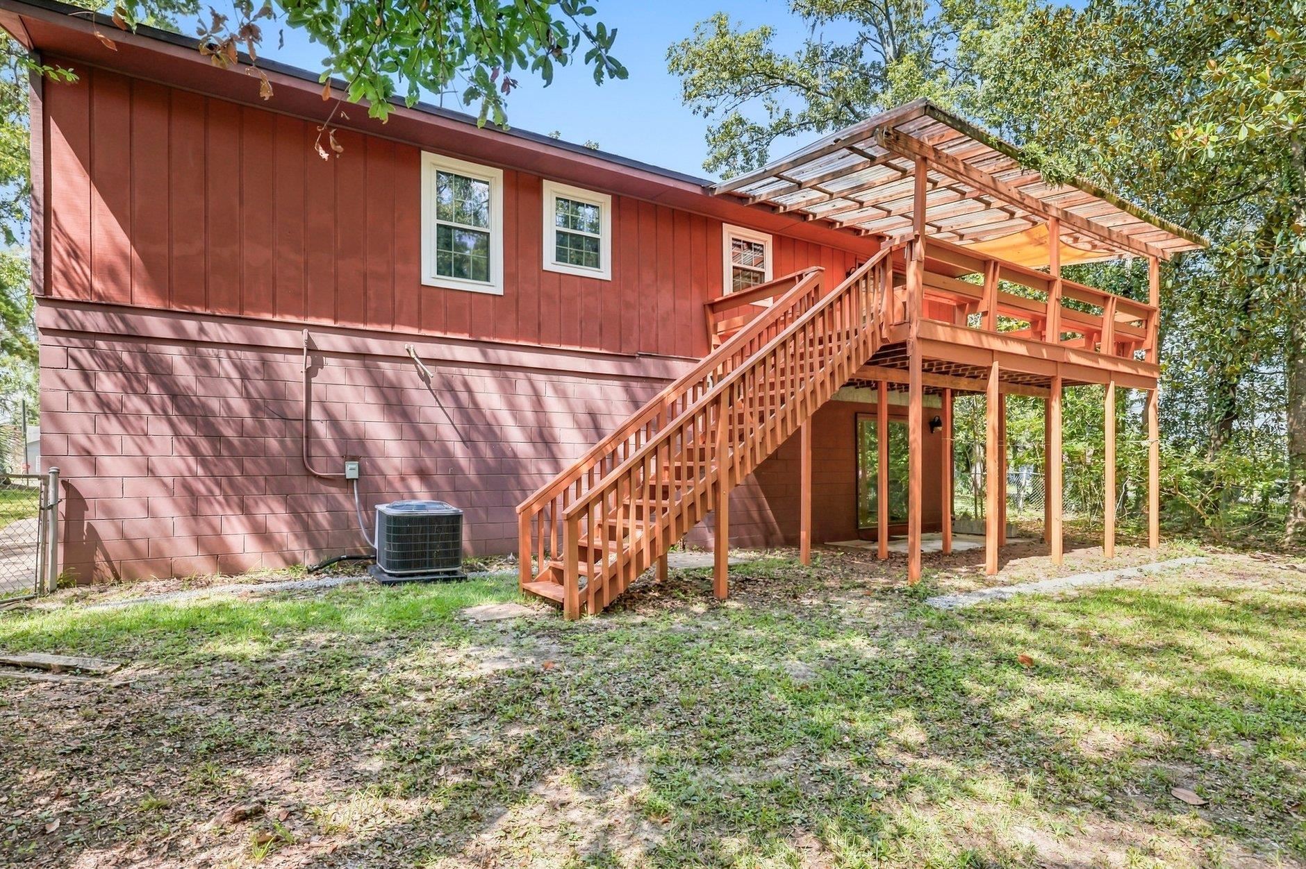 Rear of a red home with an elevated wooden deck, long staircase, and covered pergola.