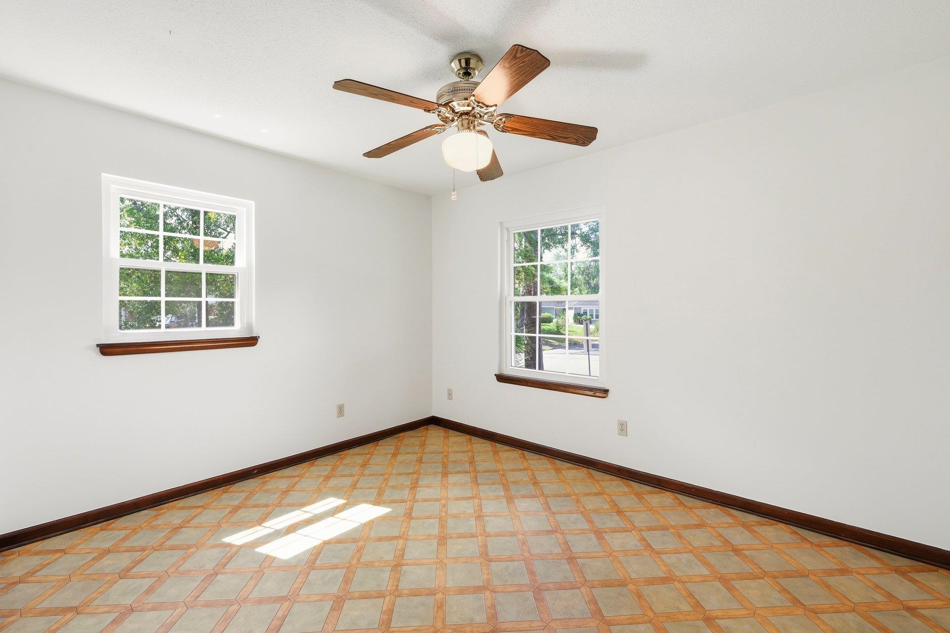 Empty room with patterned tile flooring, two windows, and a wood-blade ceiling fan.