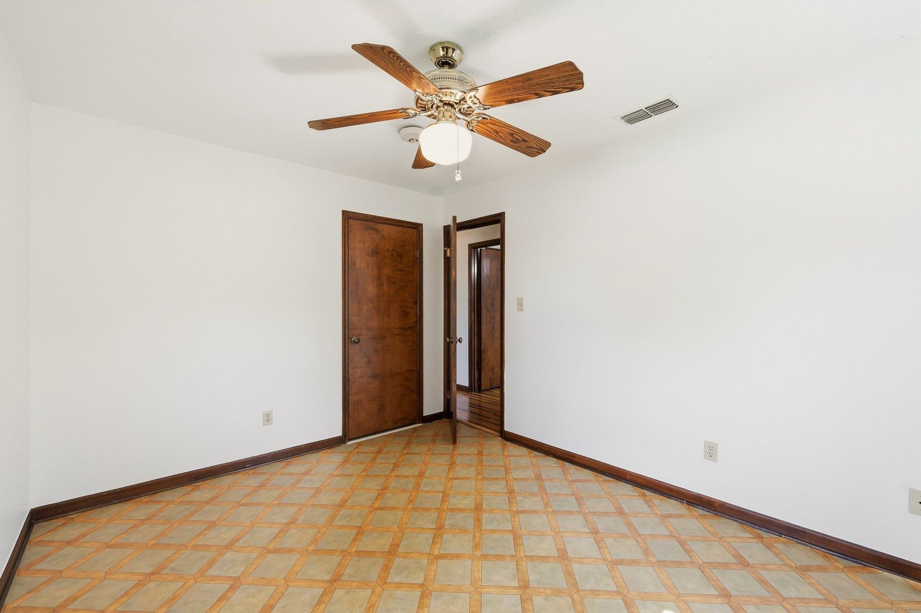 Empty room with geometric tile flooring, dark wood doors, and a ceiling fan.