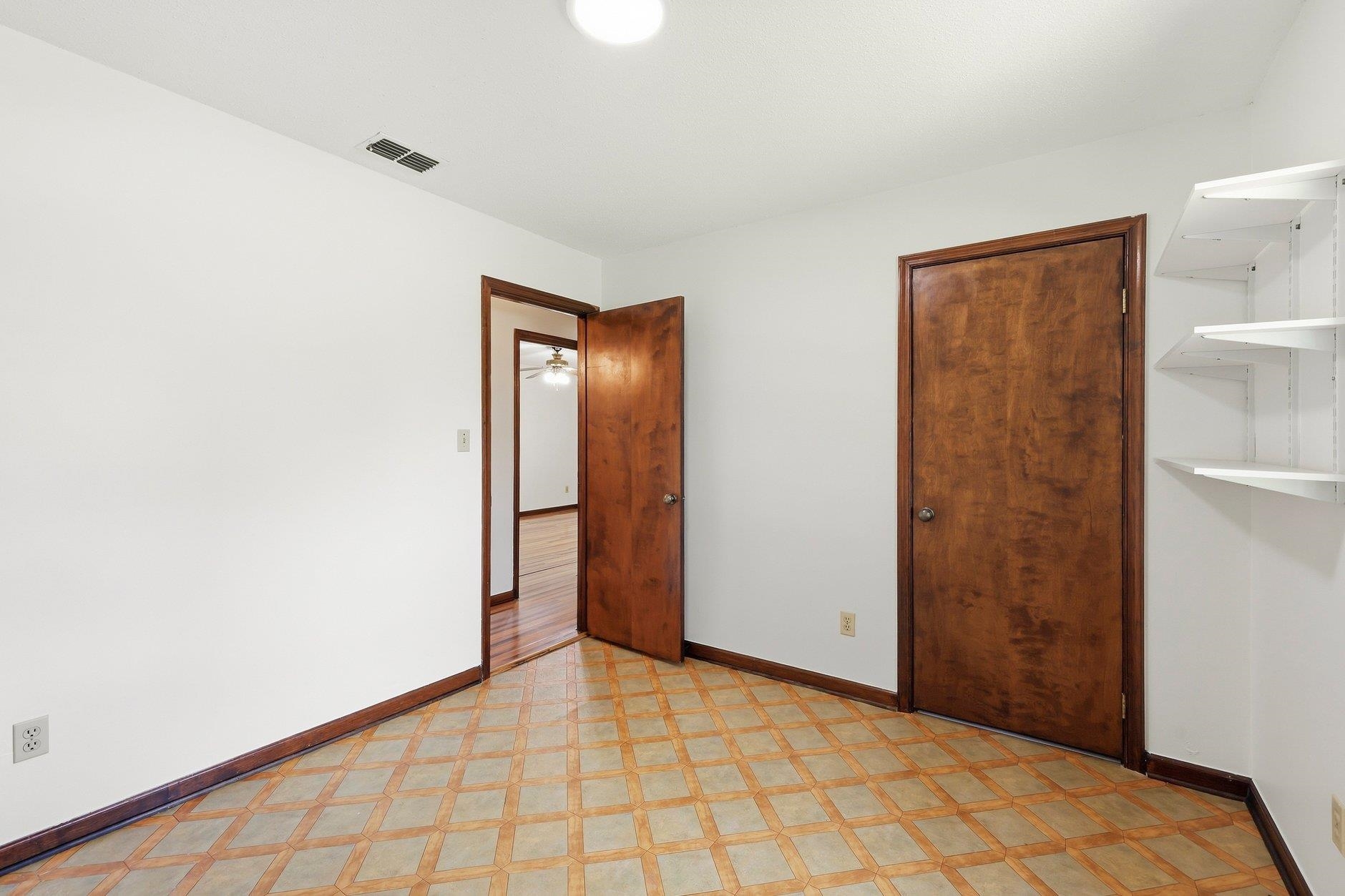 Empty room with patterned tile flooring, built-in white shelves, and dark wood doors.