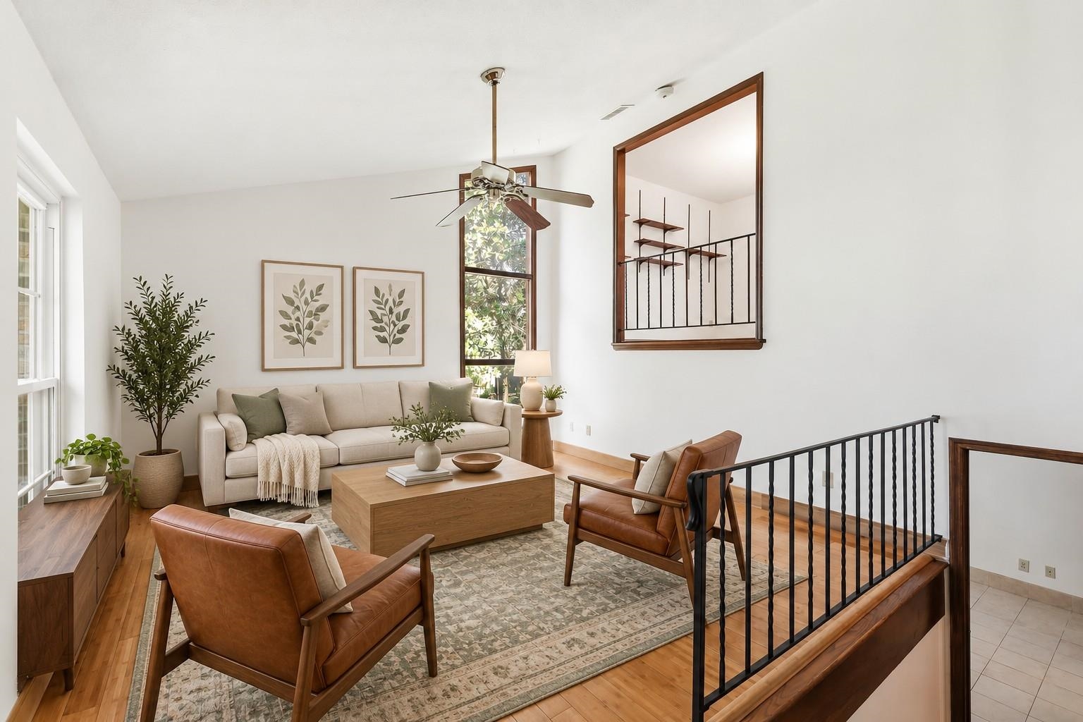 Living room with leather armchairs, wood floors, a tall window, and an open staircase.